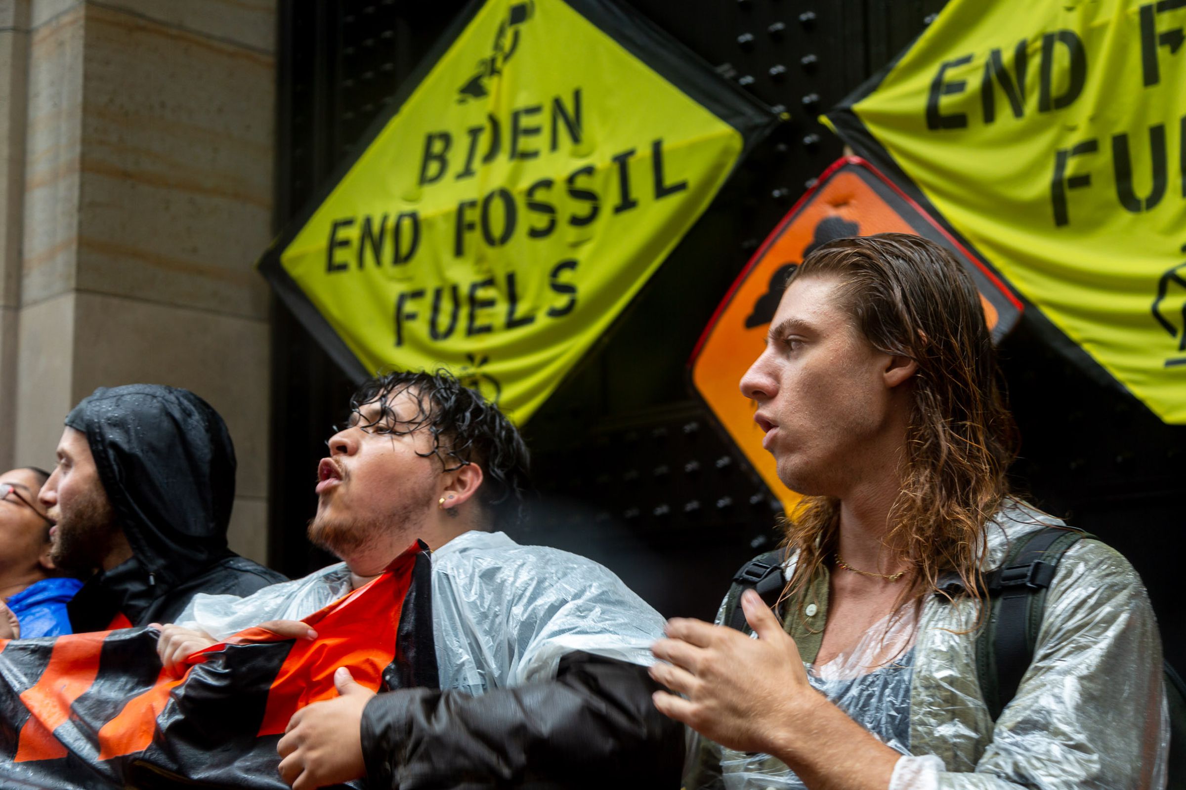 People singing in front of a sign that says ‘Biden End Fossil Fuels’