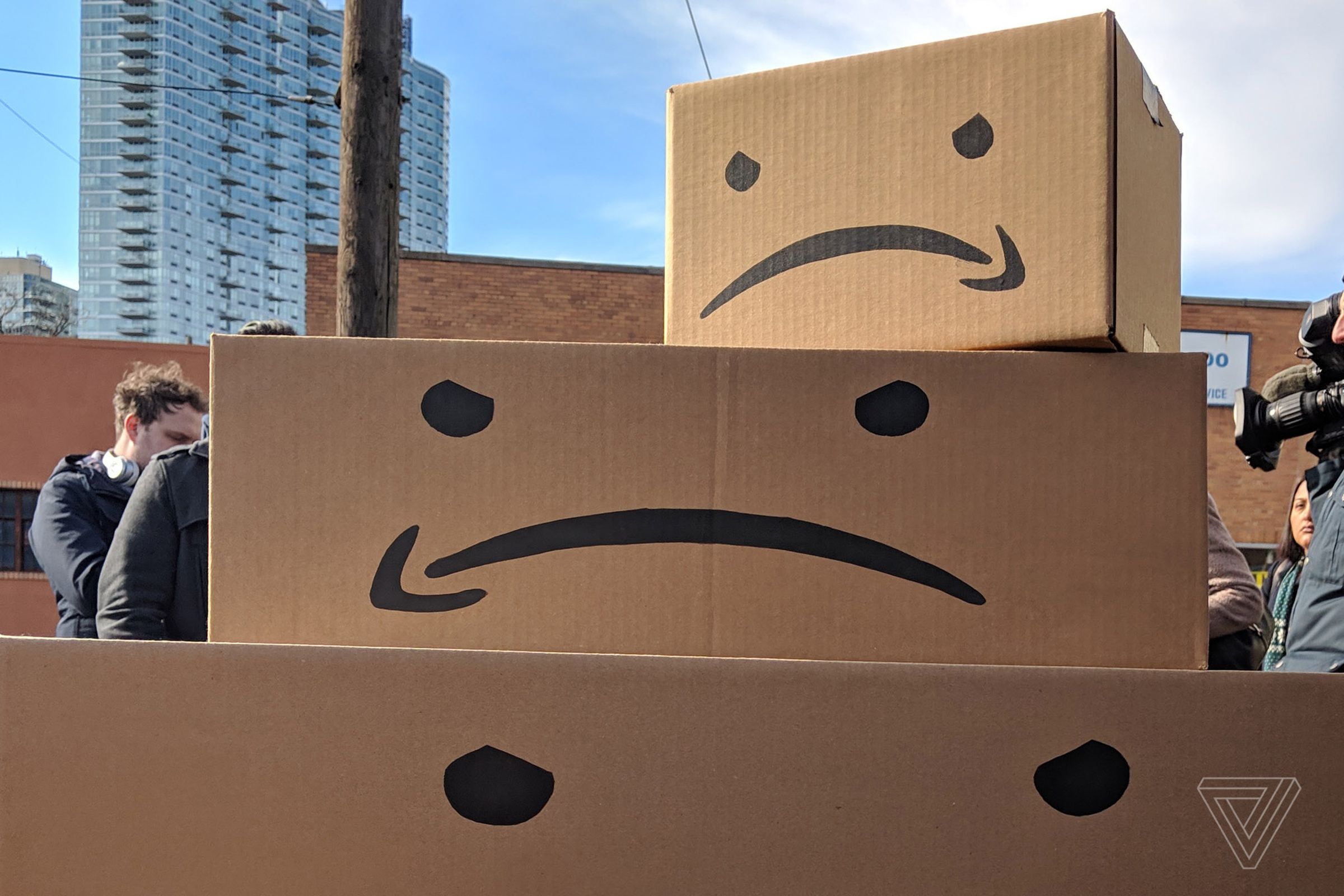 Image of three cardboard boxes stacked on top of each other, with frowning faces using an upside-down amazon logo for the mouth printed on them.