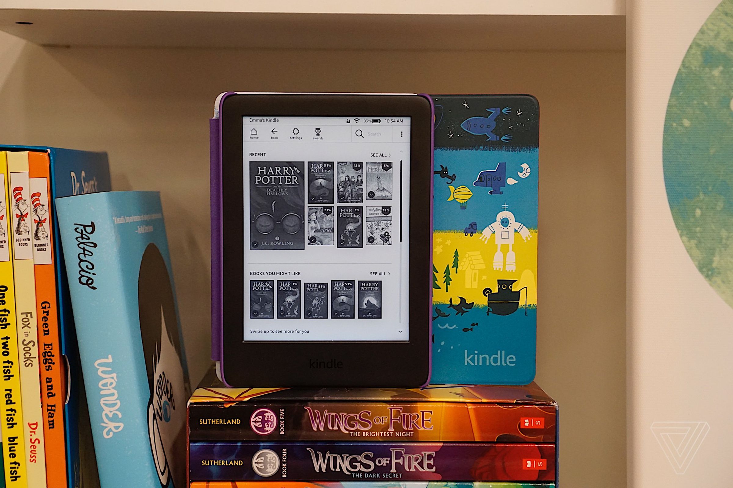 Kindle on bookshelf with hardcovers.