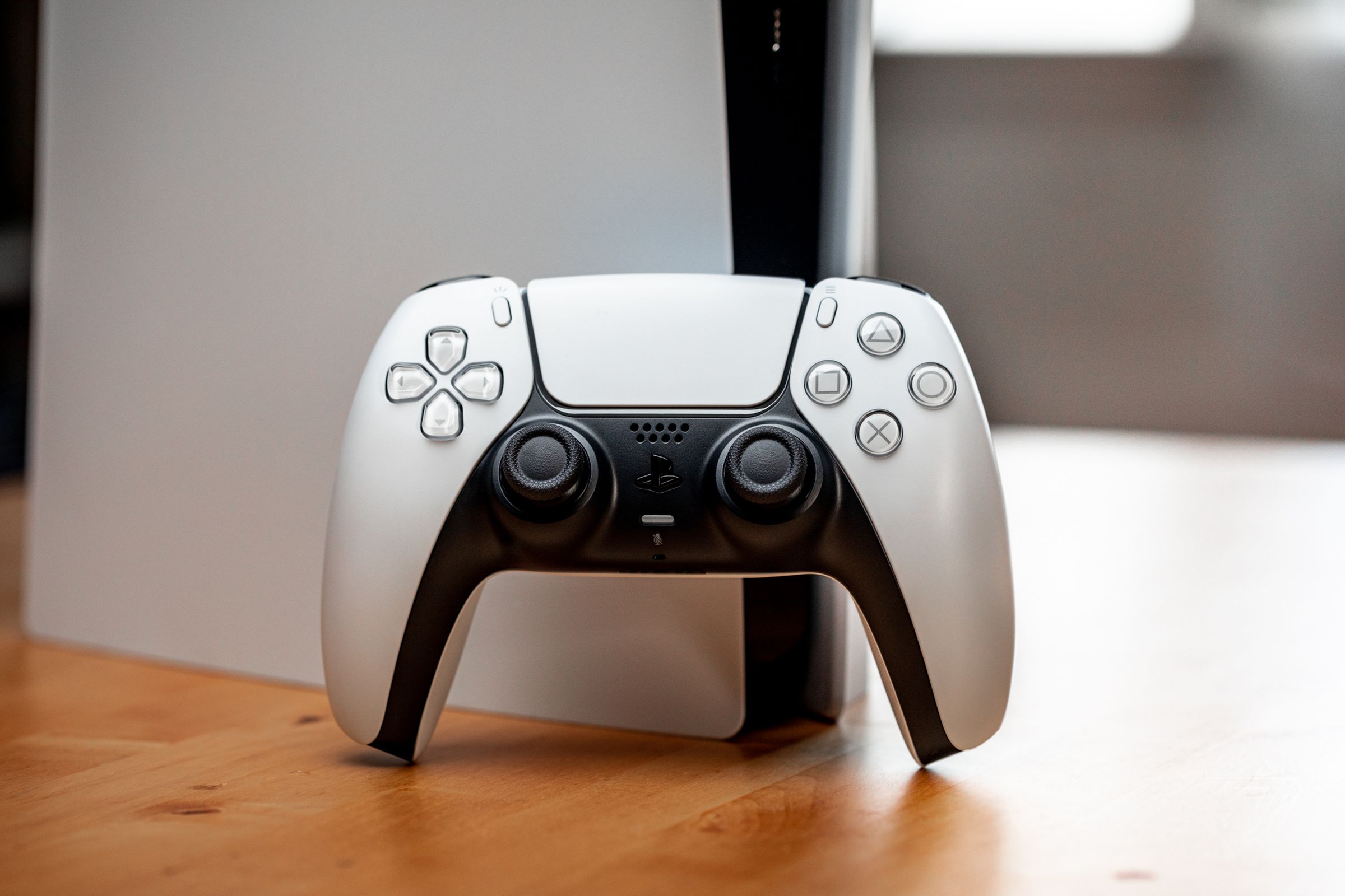 A Sony DualSense controller facing forward and resting against the front of a PlayStation 5 console.