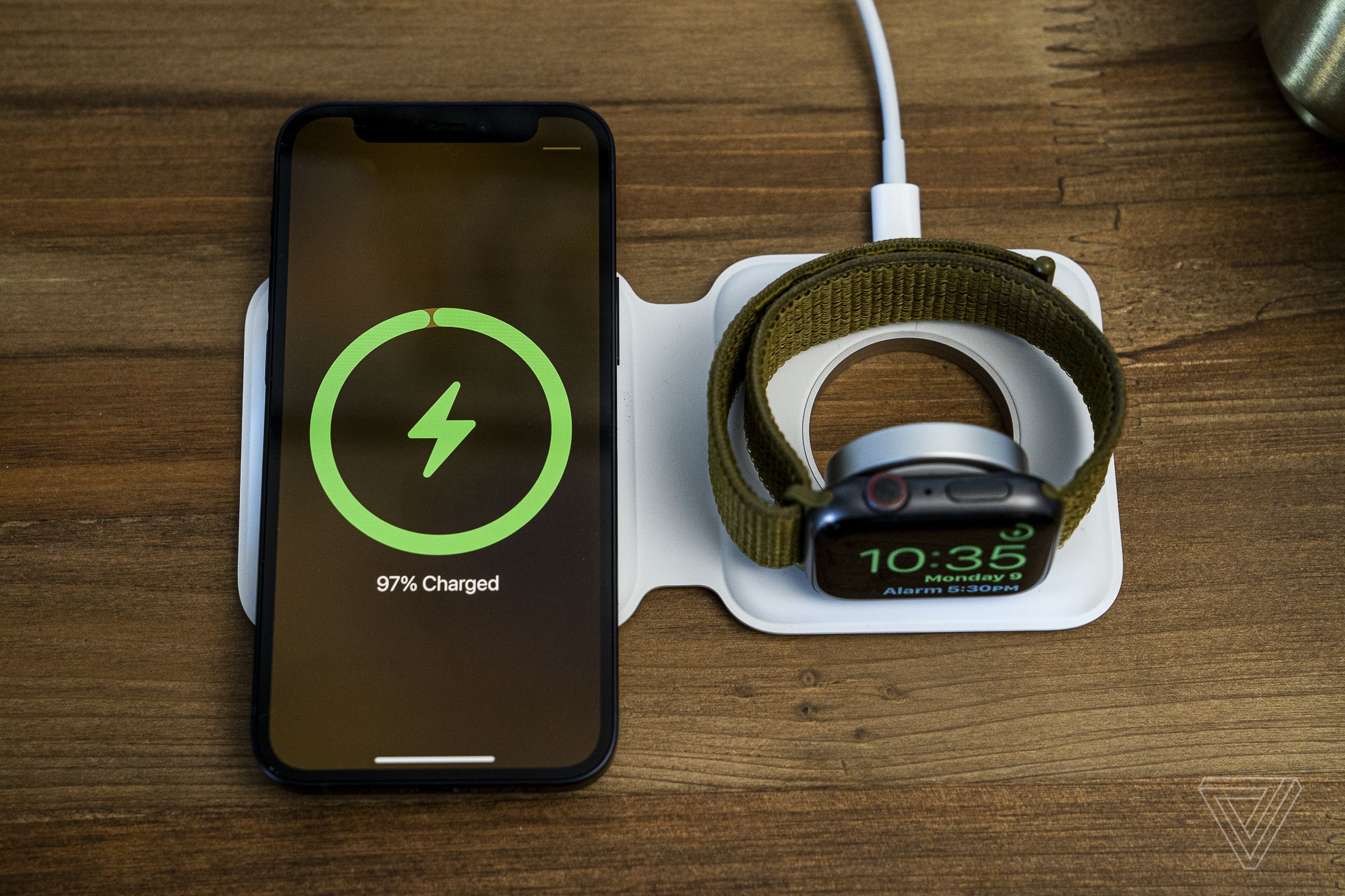 An iPhone and Apple Watch charging wirelessly on an Apple MagSafe Duo Charger, atop a wood table.