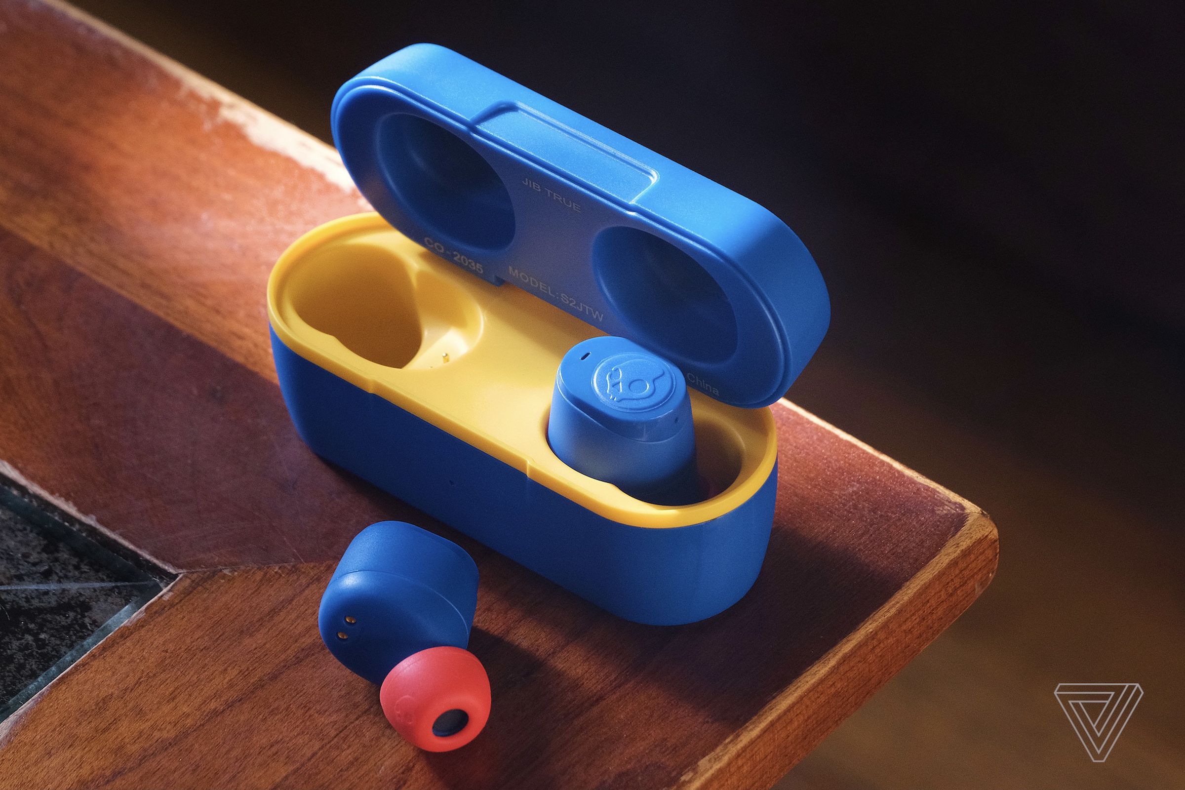 The colorful blue and red Skullcandy Jib True Wireless earbuds, pictured on a table in their blue and yellow charging case.