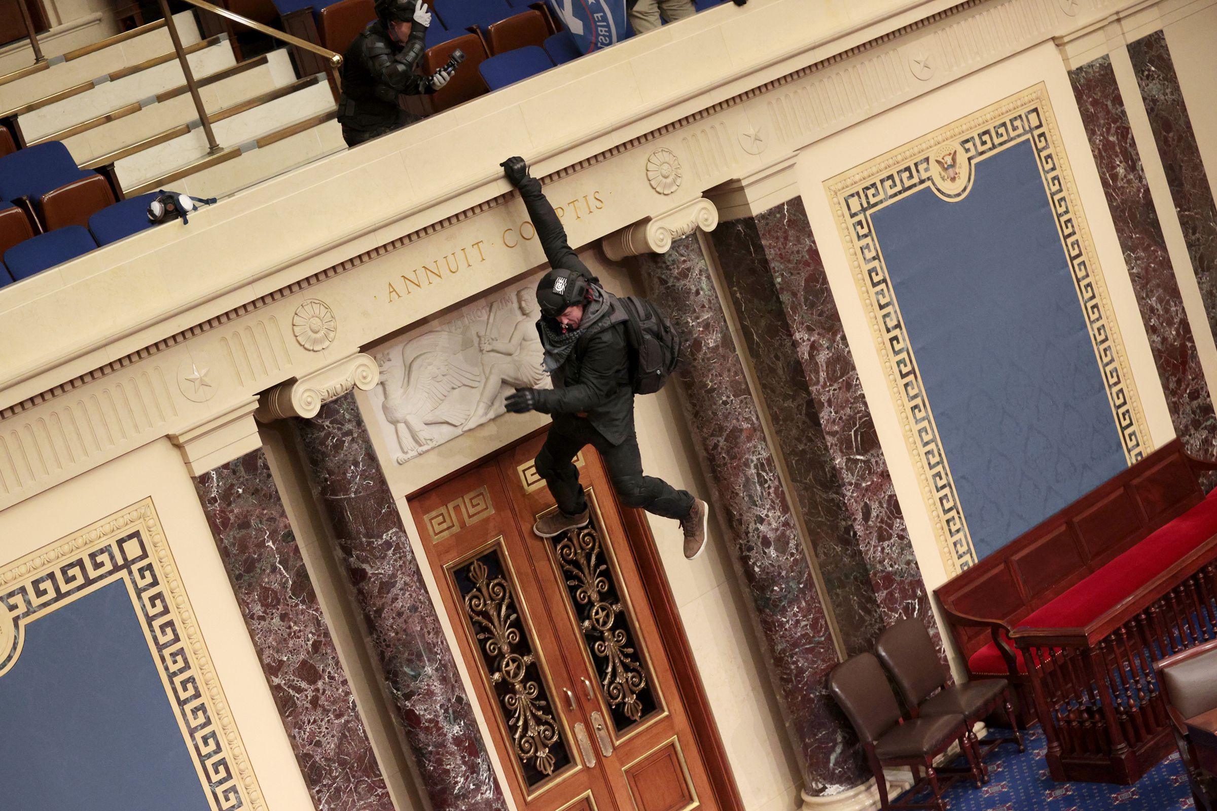 An intruder hangs from the Senate balcony, attempting to drop to the lower level.
