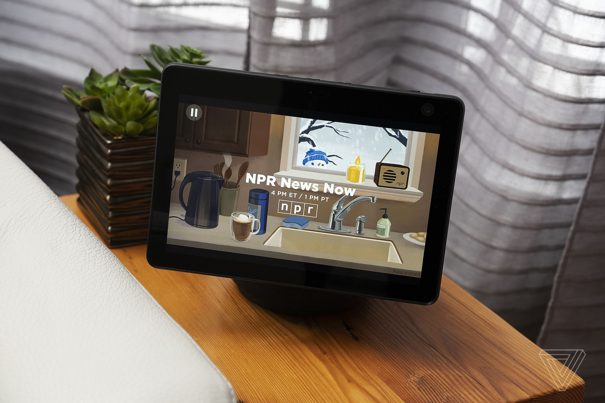 An Echo Show 10 device sitting on a piece of wood furniture beside a couch.