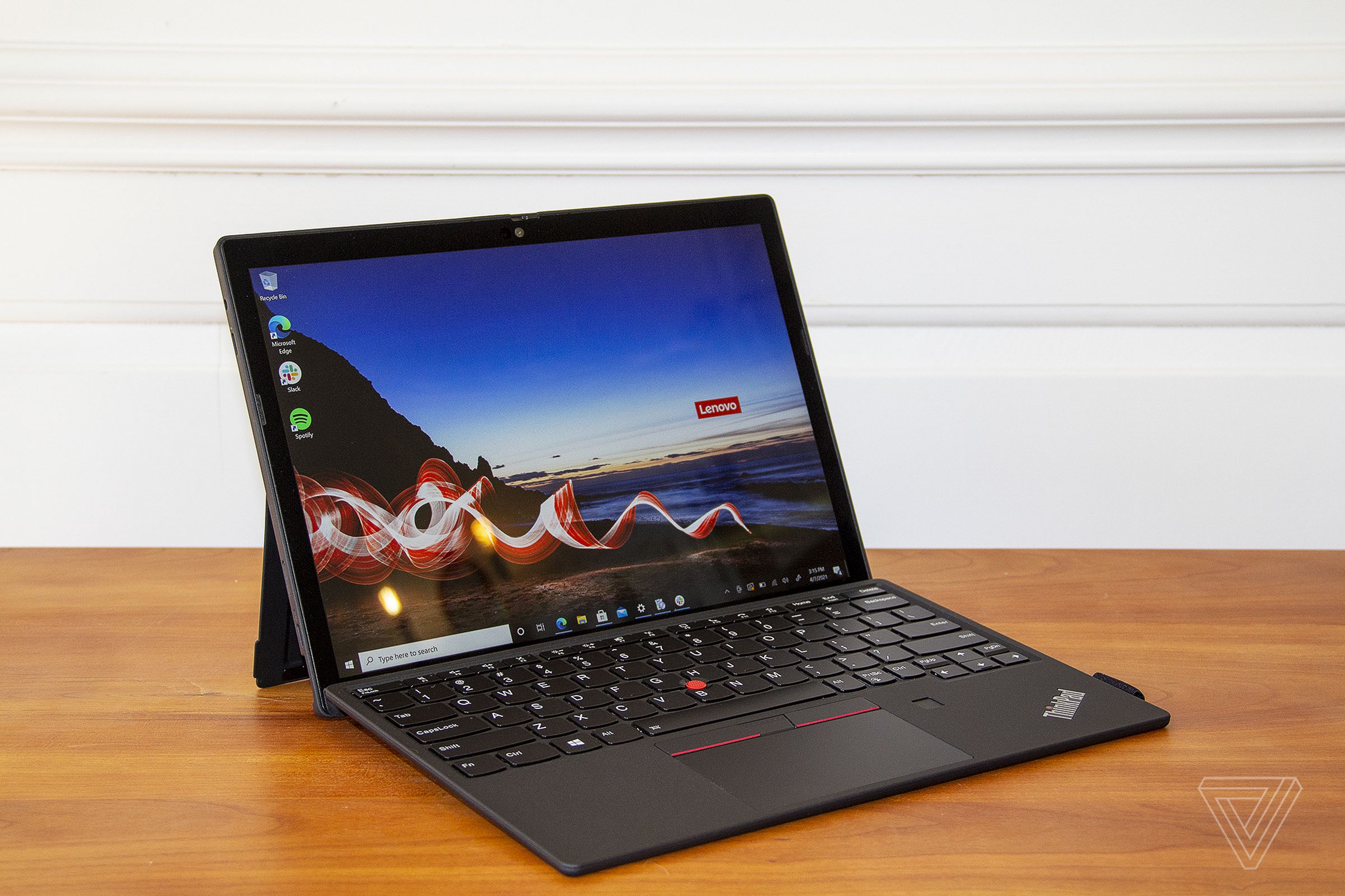 The ThinkPad X12 Detachable open from the front, angled to the right. The screen displays a beach with a red ribbon across it and the Lenovo logo on the horizon. 