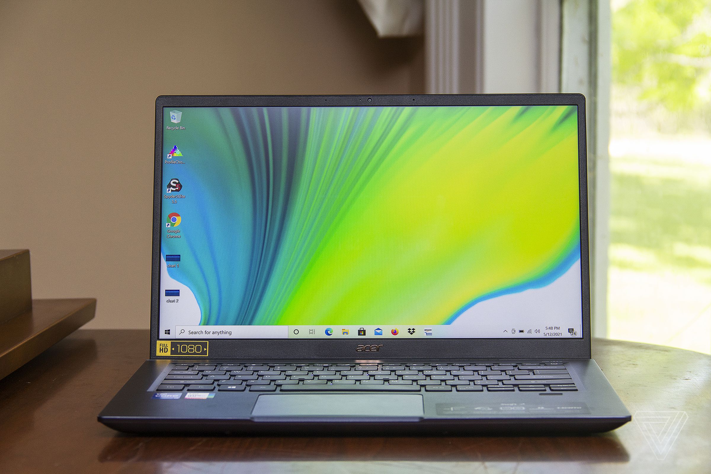 The Acer Swift 3X open on a piano seen from the front. The screen displays a blue, green, and white gradient.