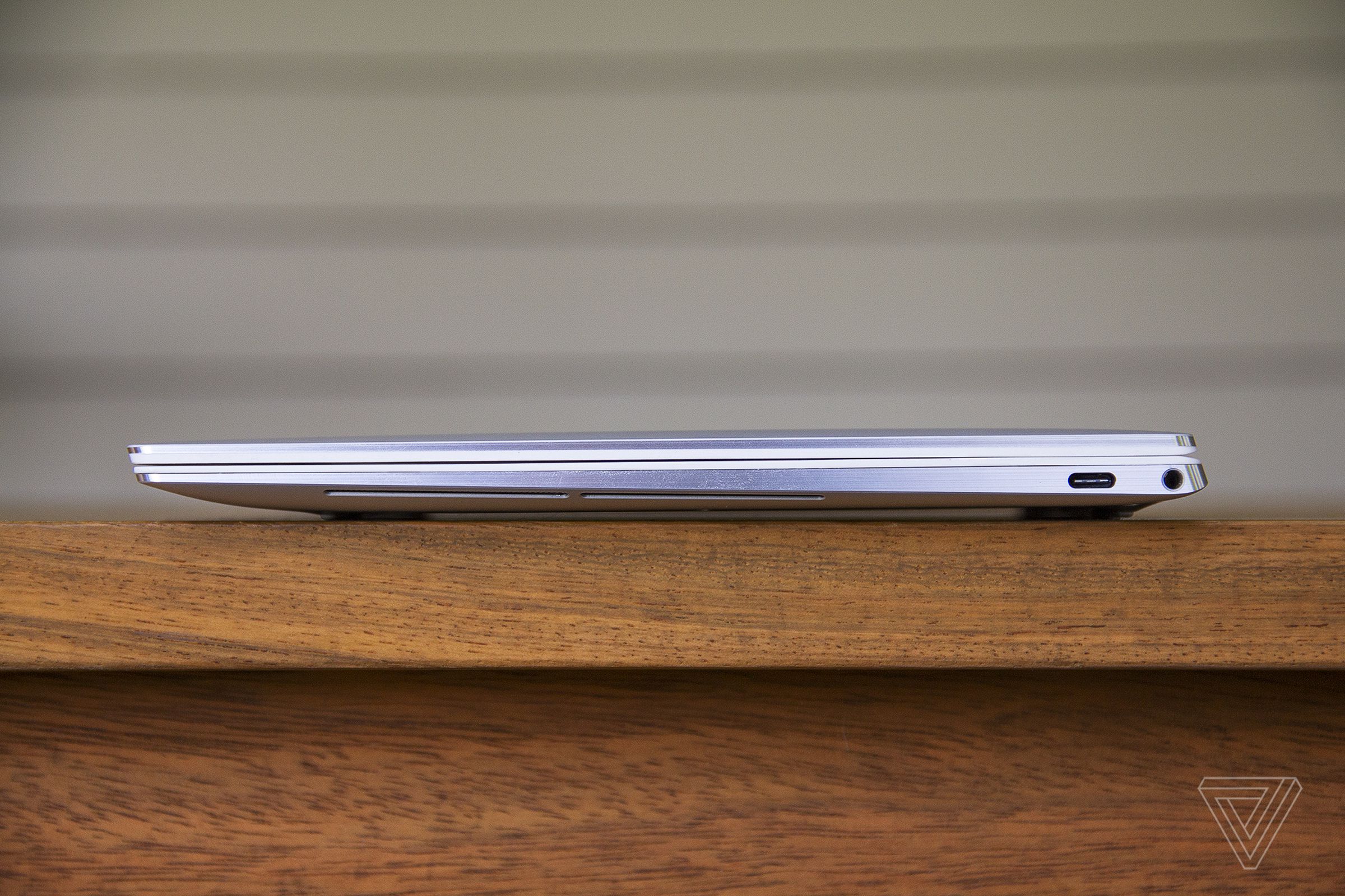 The Dell XPS 13 OLED closed seen from the left side on a wooden table.