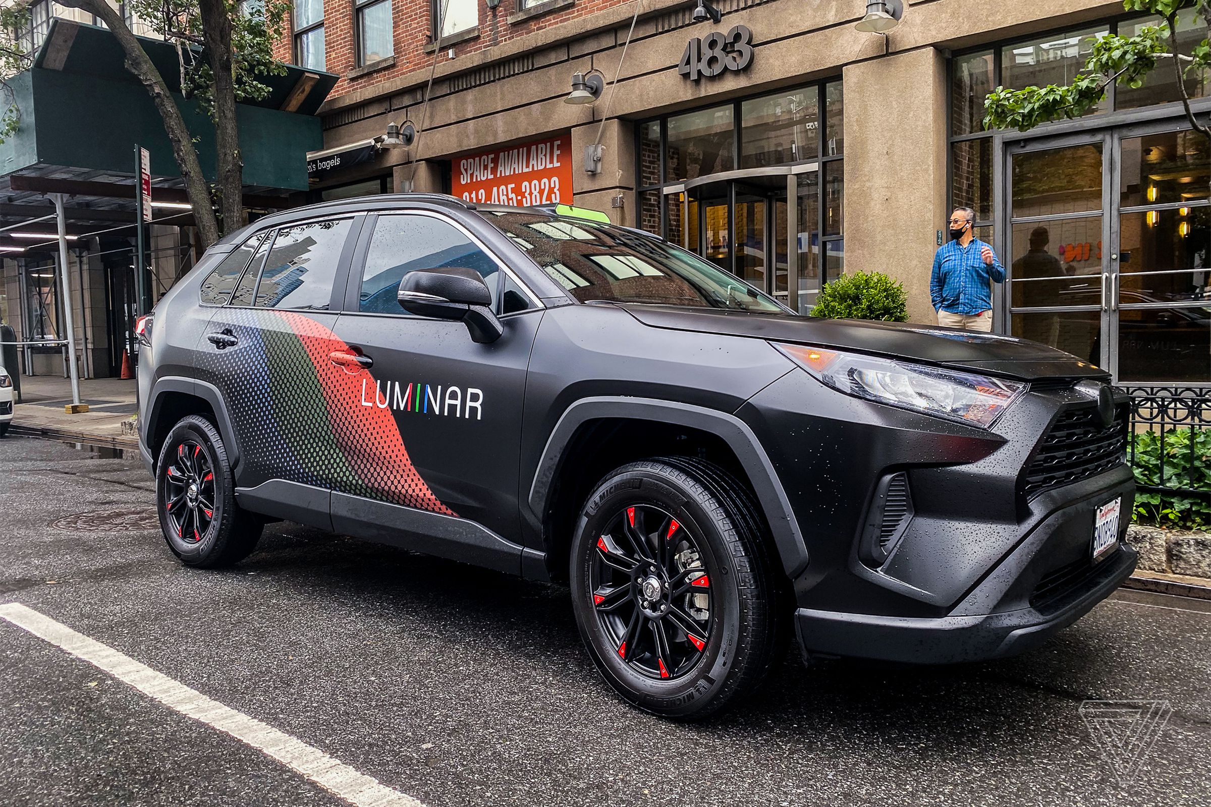 a black SUV is on a city street with the Luminar logo printed on its side.