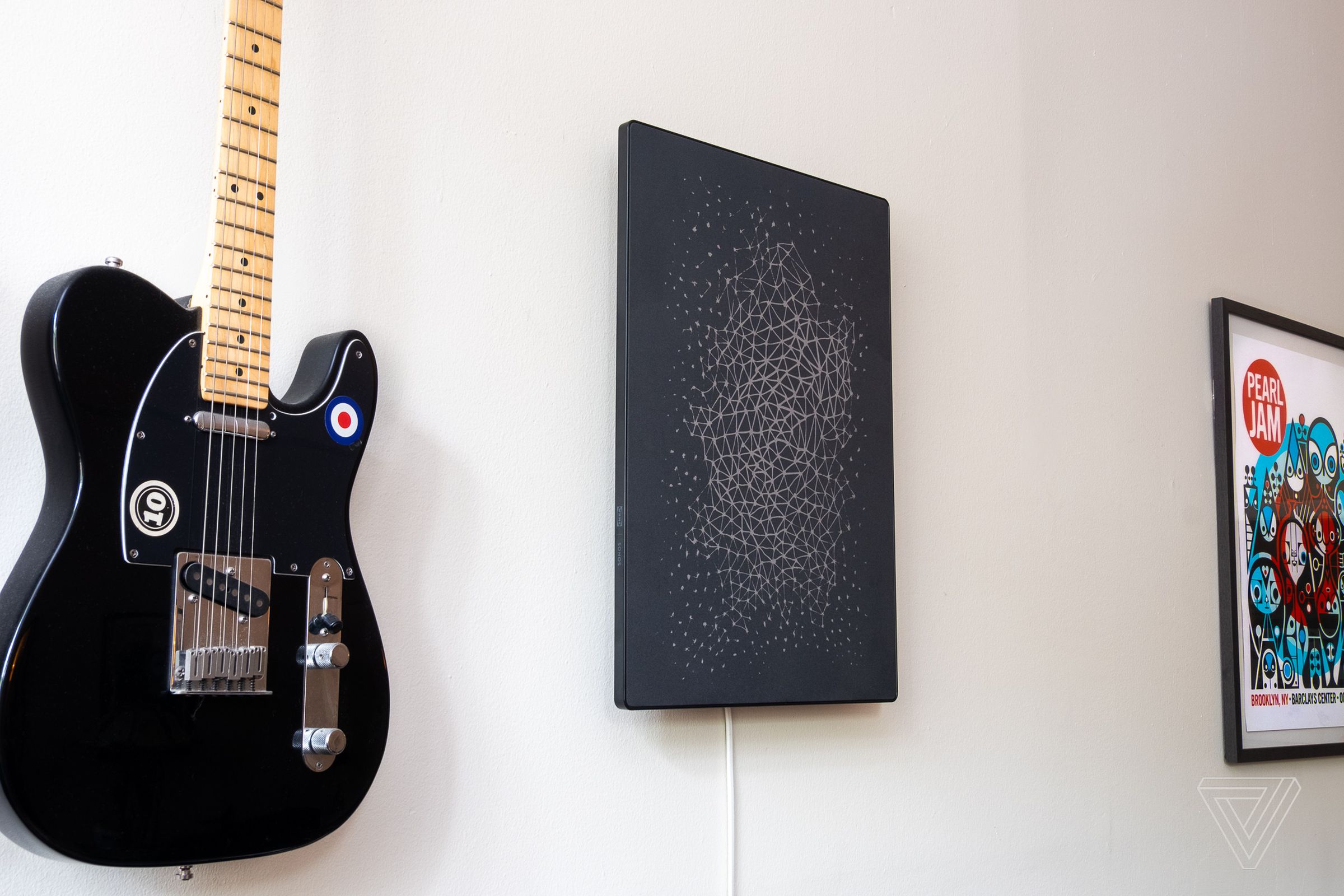 A photo of the Ikea Symfonisk Picture Frame Speaker on a wall next to a guitar and concert poster.