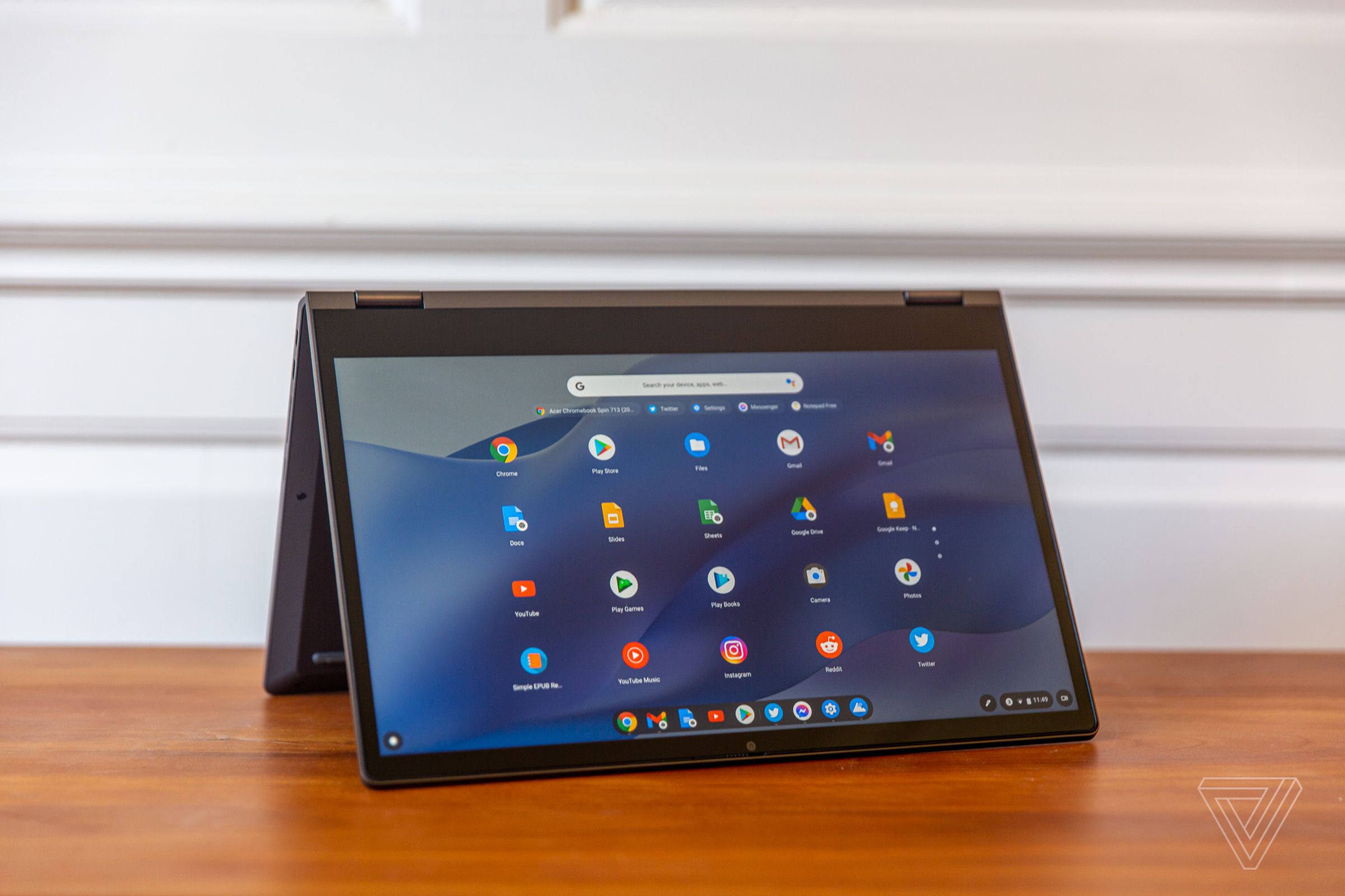 The Lenovo Flex 5 Chromebook in tent mode, angled to the right. The screen displays a grid of Chrome OS apps on a blue wavy background.