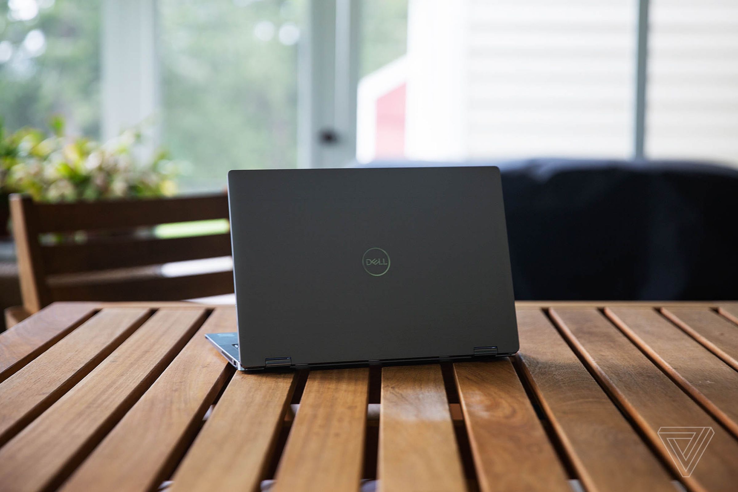 The Dell Latitude 9420 facing away from the camera, angled slightly to the left, on a porch table.