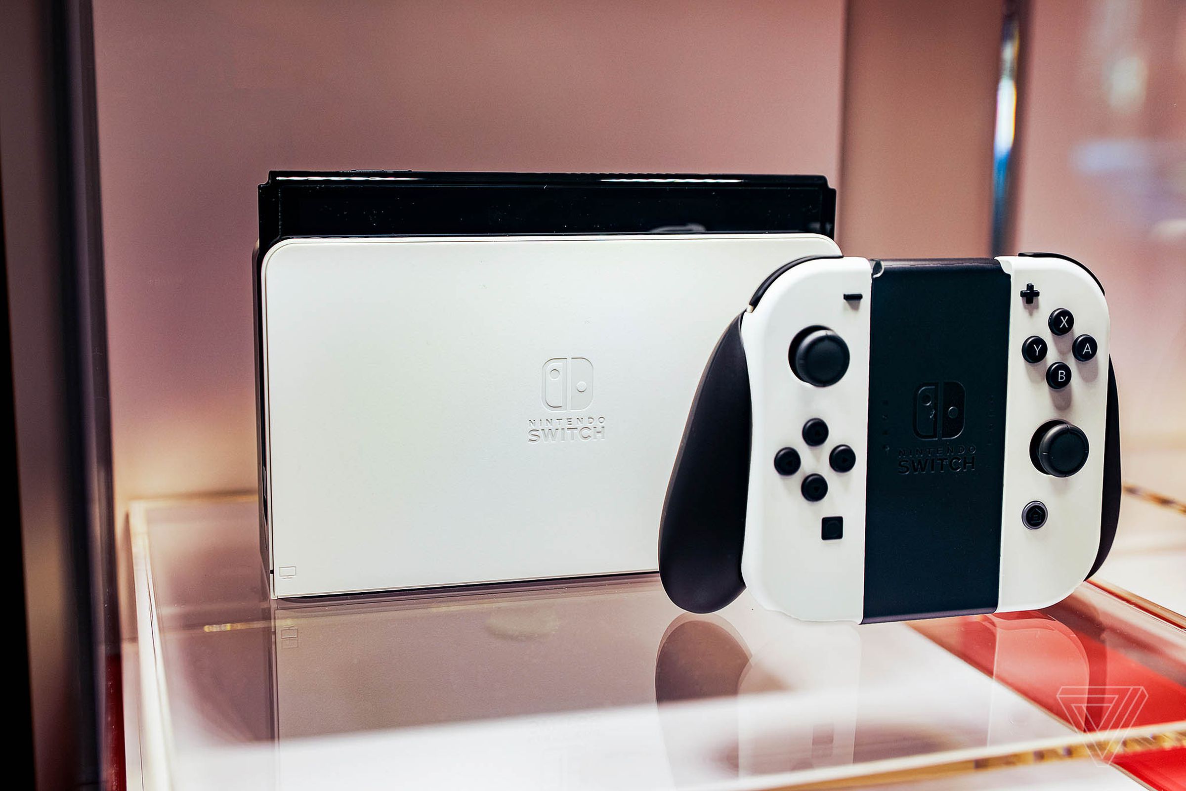 A docked Nintendo Switch OLED model sitting on a piece of glass next to its controller.