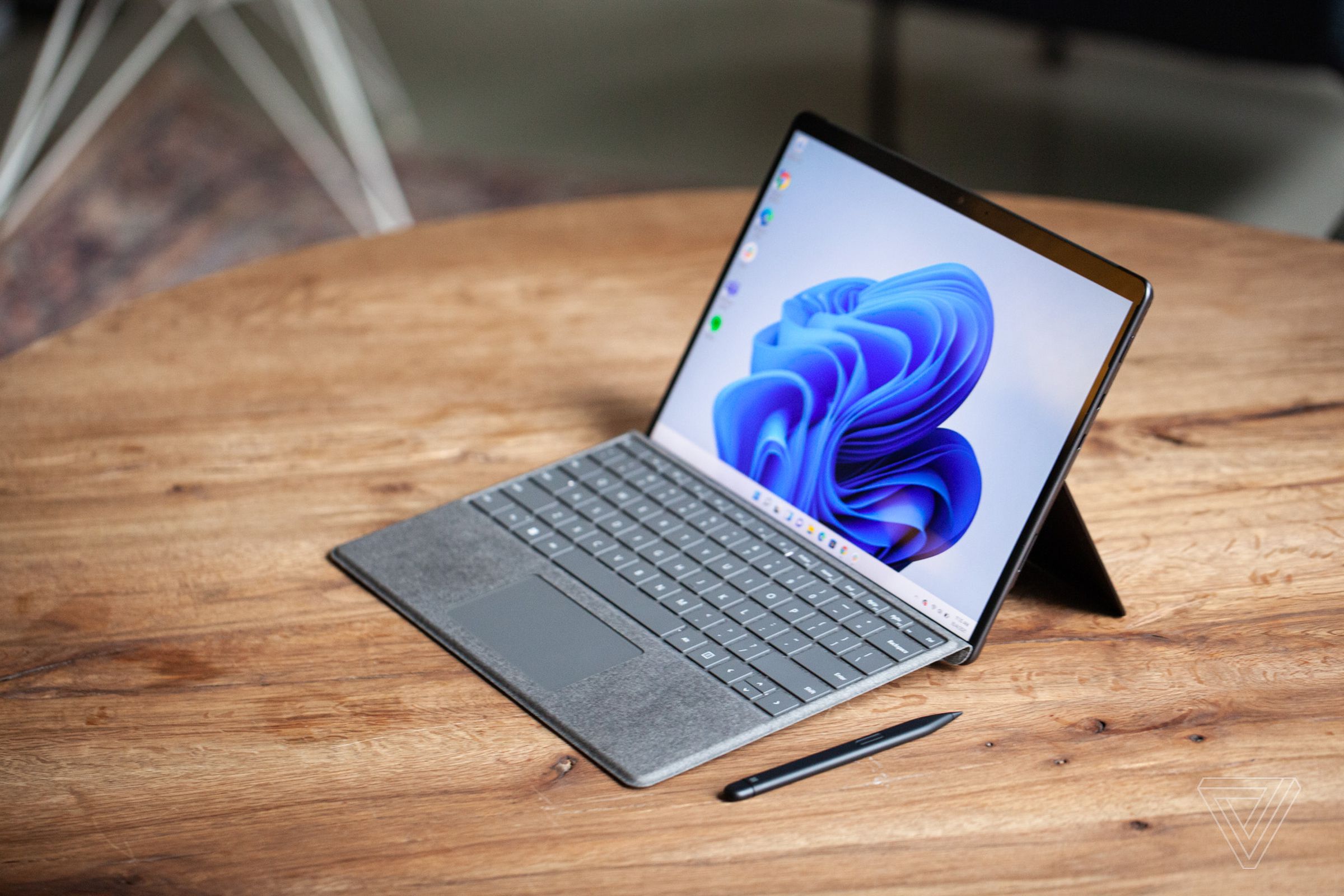 The Surface Pro 8 seen from above and to the right on a table with the Surface Slim Pen 2 next to it and Signature Keyboard attached. The screen displays a blue swirl on a white background.