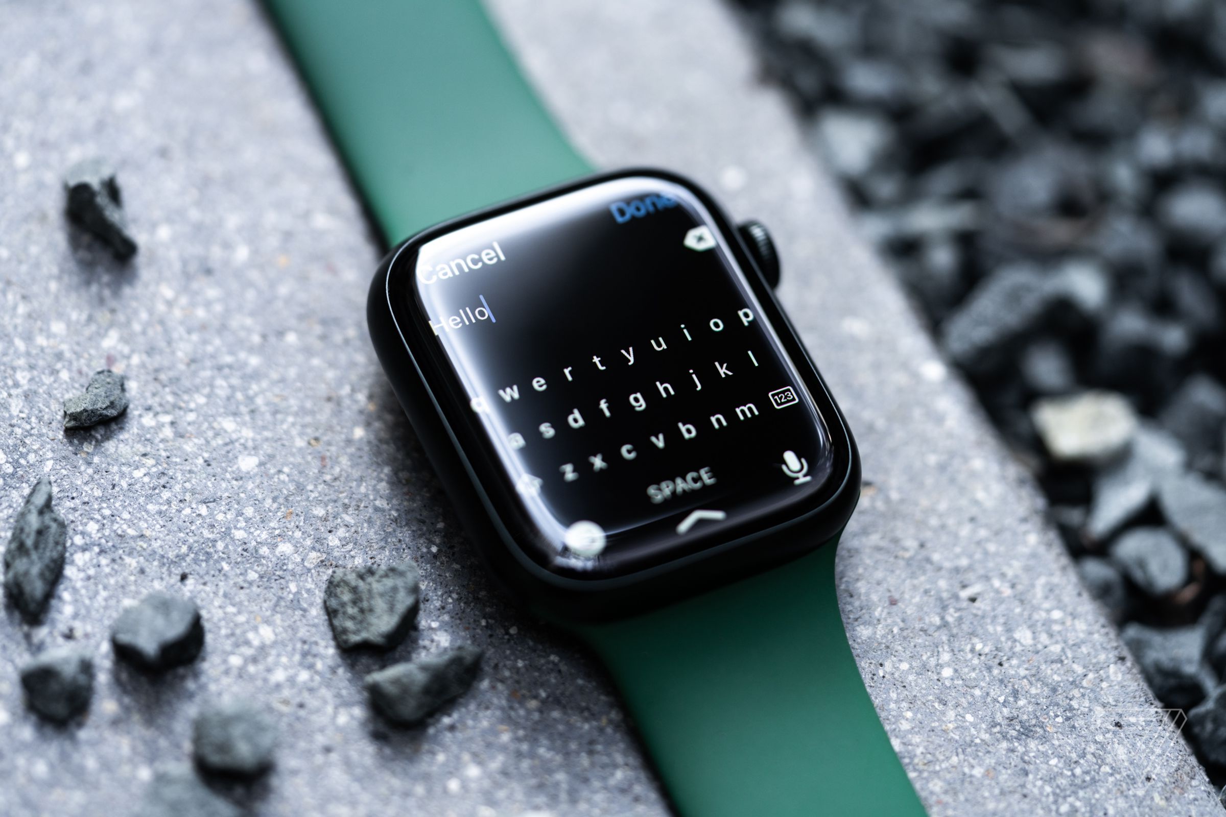 An Apple Watch on a stone surface, with a keyboard typing the word “hello.”