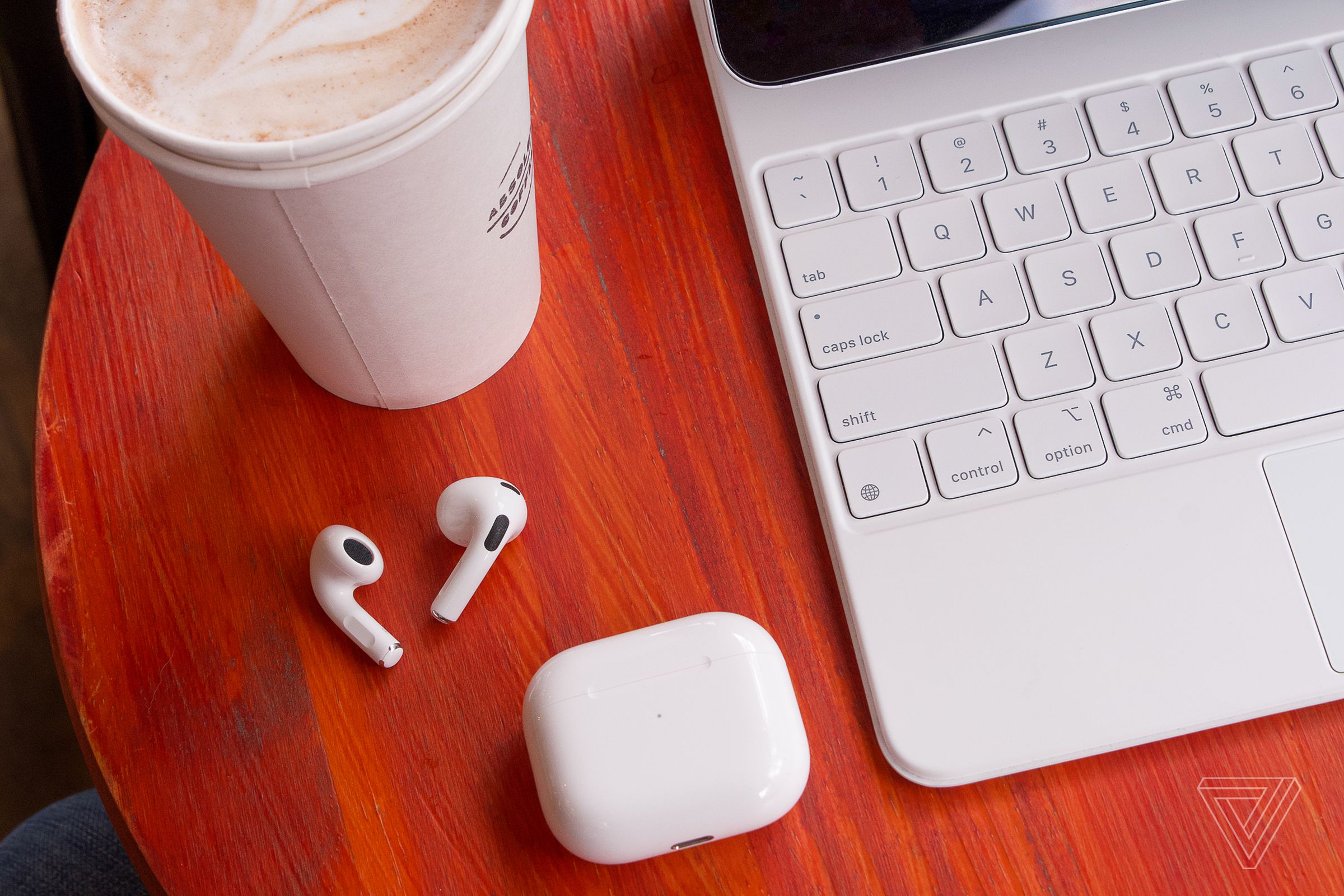 An image of Apple’s AirPods on a table beside a cup of coffee.