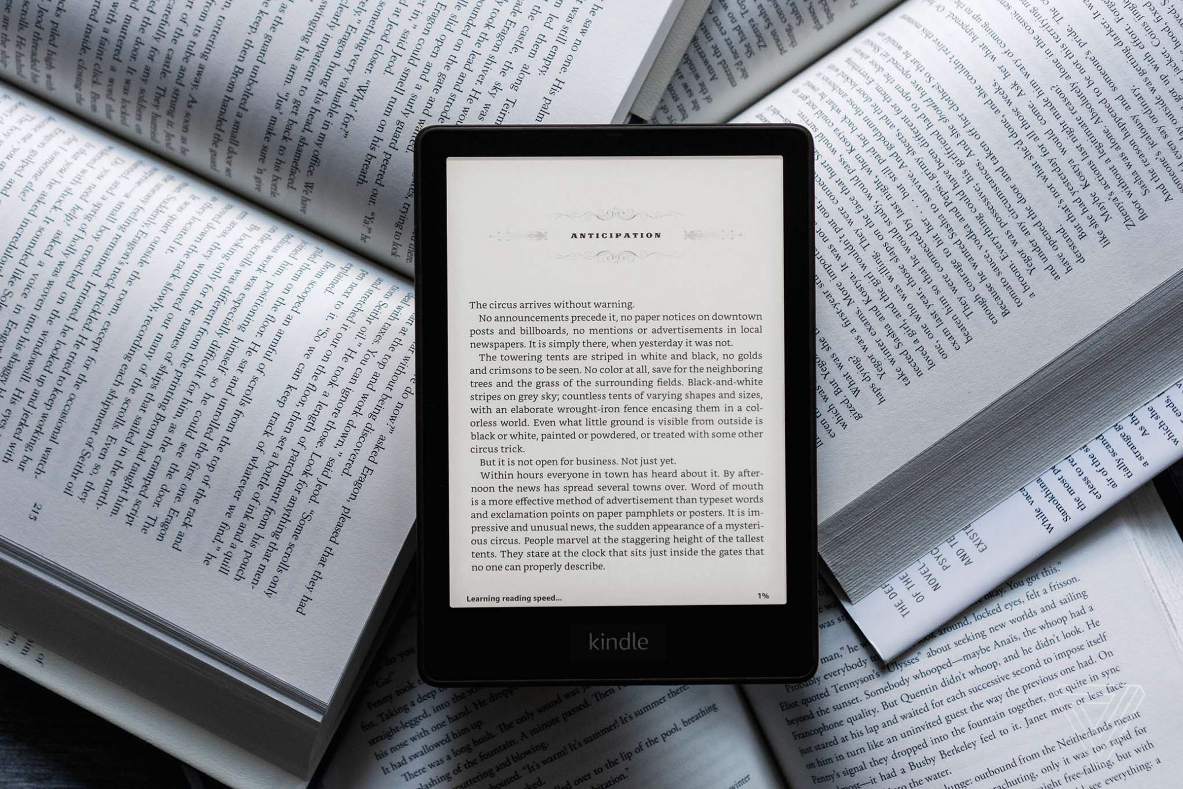 جهاز Kindle Paperwhite مستلقي على مجموعة من الكتب المادية أثناء تشغيله.