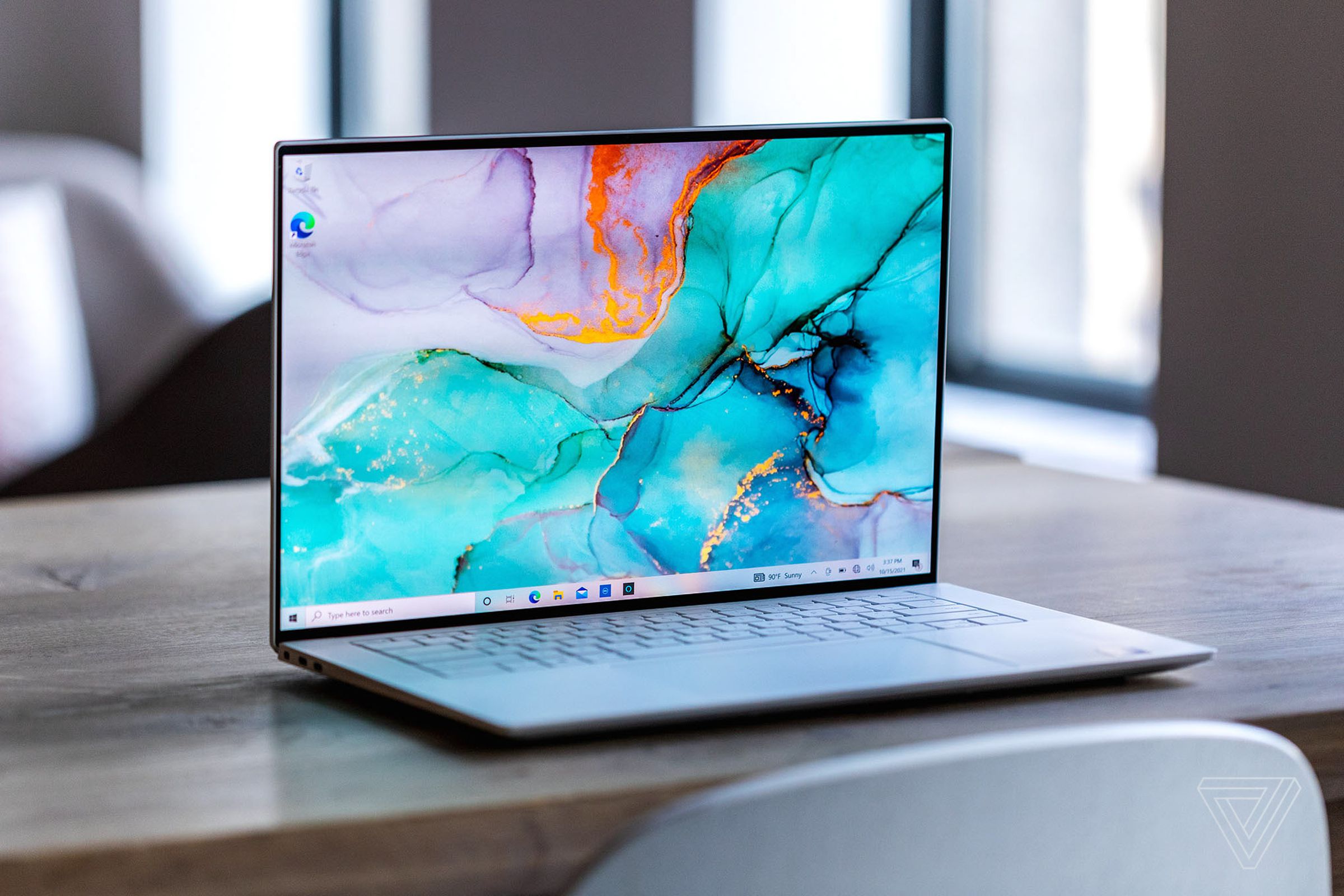The Dell XPS 15 open on a wooden table. The screen displays a marbled blue and purple surface.