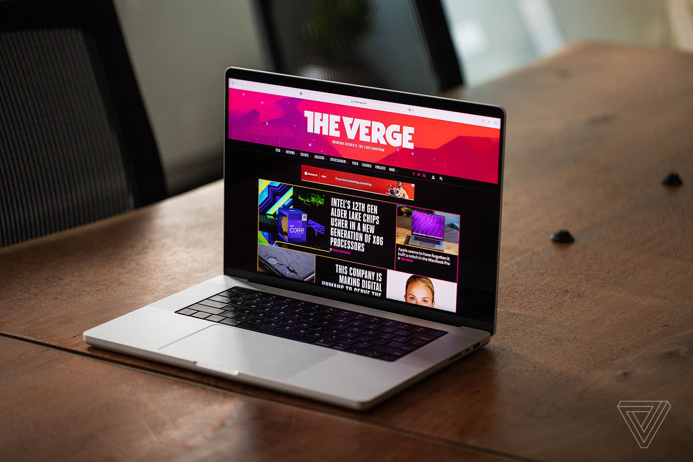 Apple’s 2021 14-inch MacBook Pro is opened on a wooden table. Its display is showing off The Verge’s homepage.