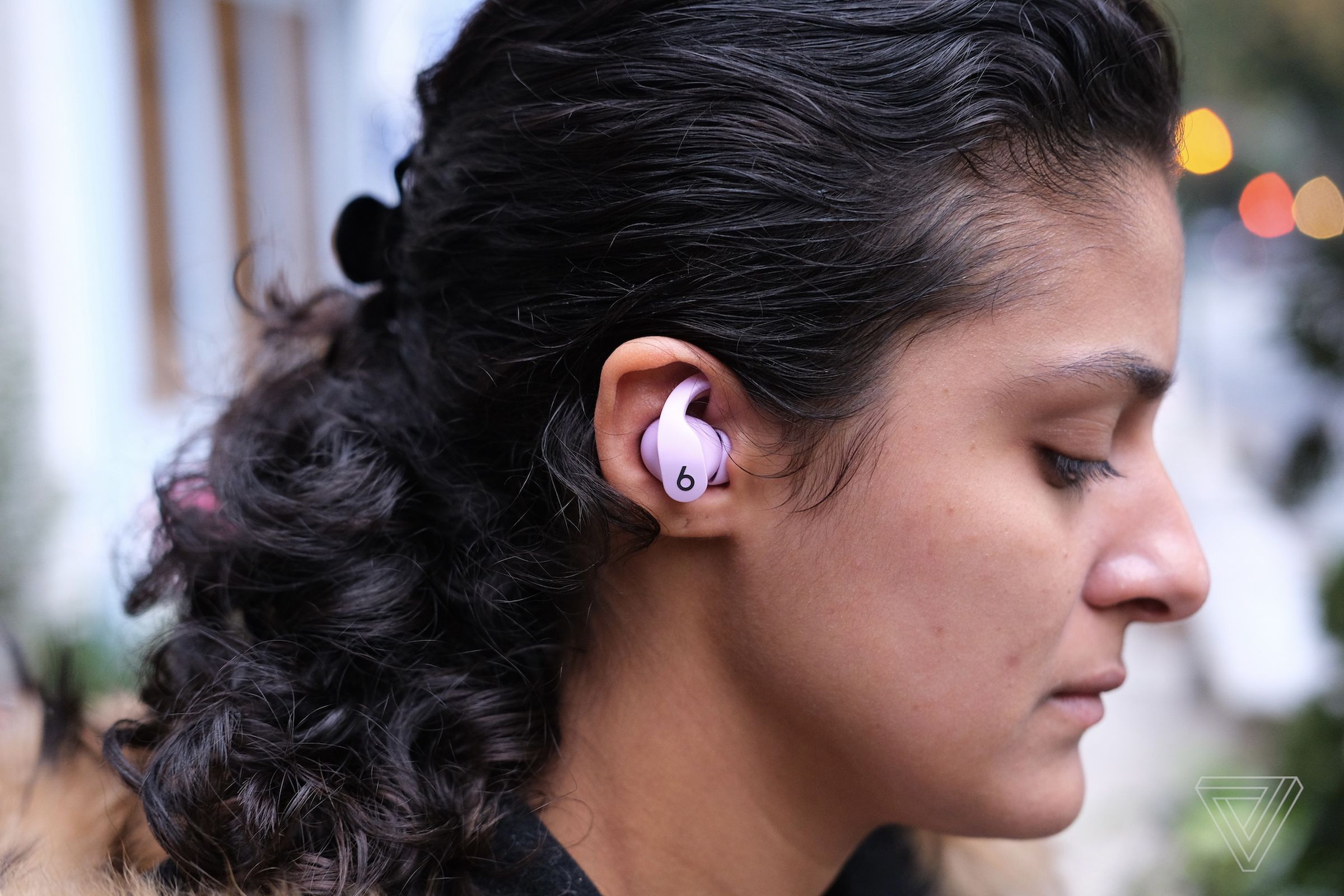 A photo of pink Beats Fit Pro earbuds in a woman’s ear.