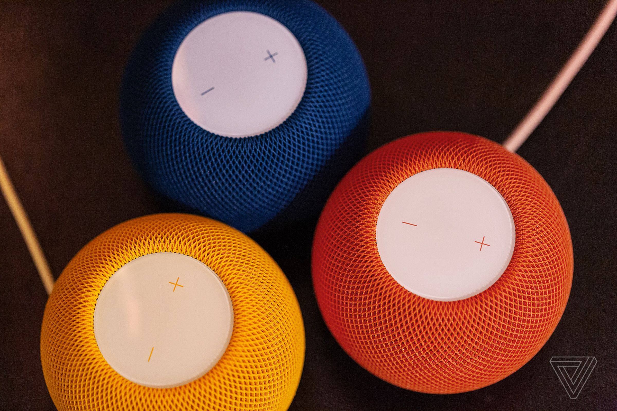A trio of blue, orange, and yellow Apple HomePod Mini speakers, sitting together on a table.