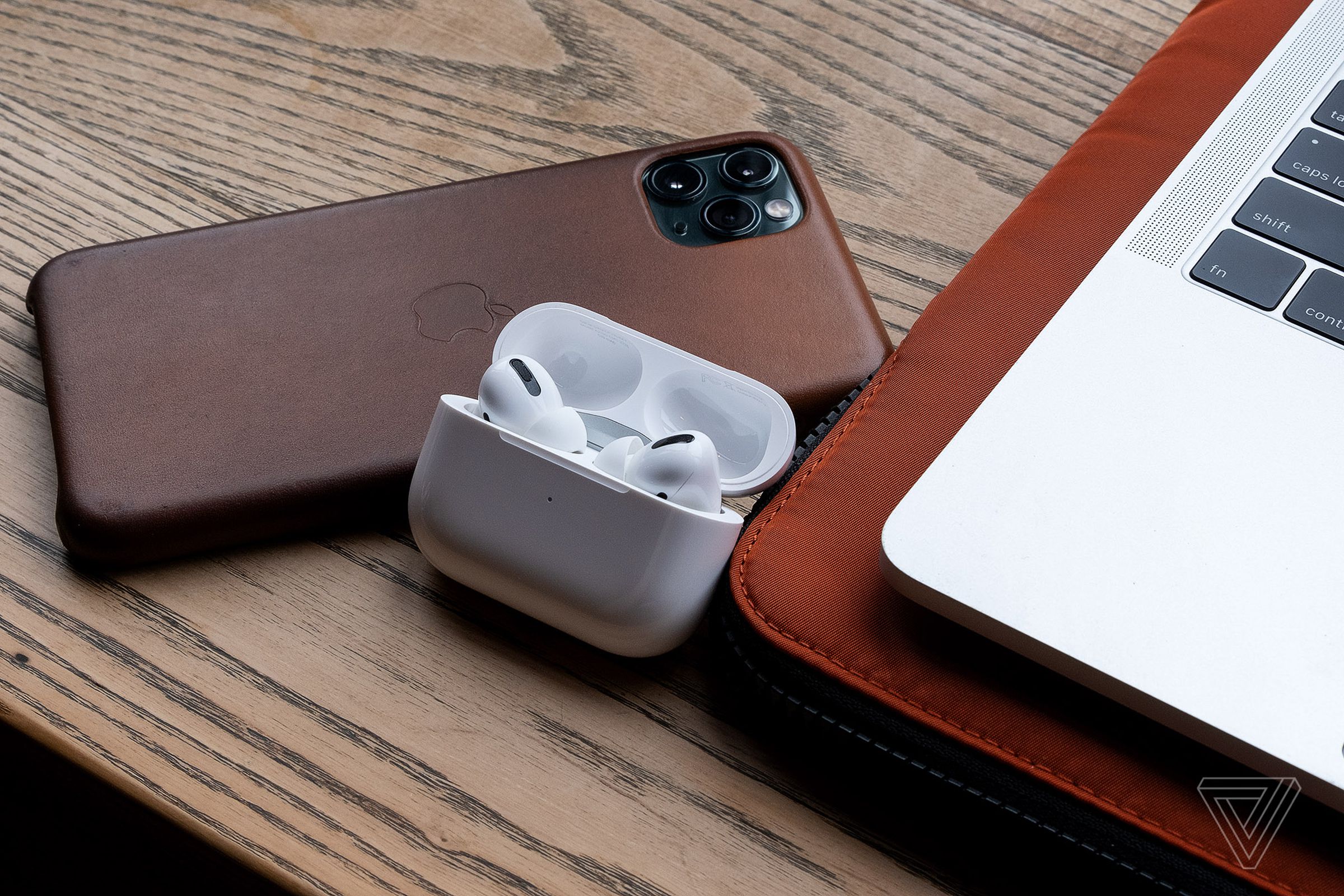 The last-gen AirPods Pro sitting on a desk near an iPhone and a MacBook.