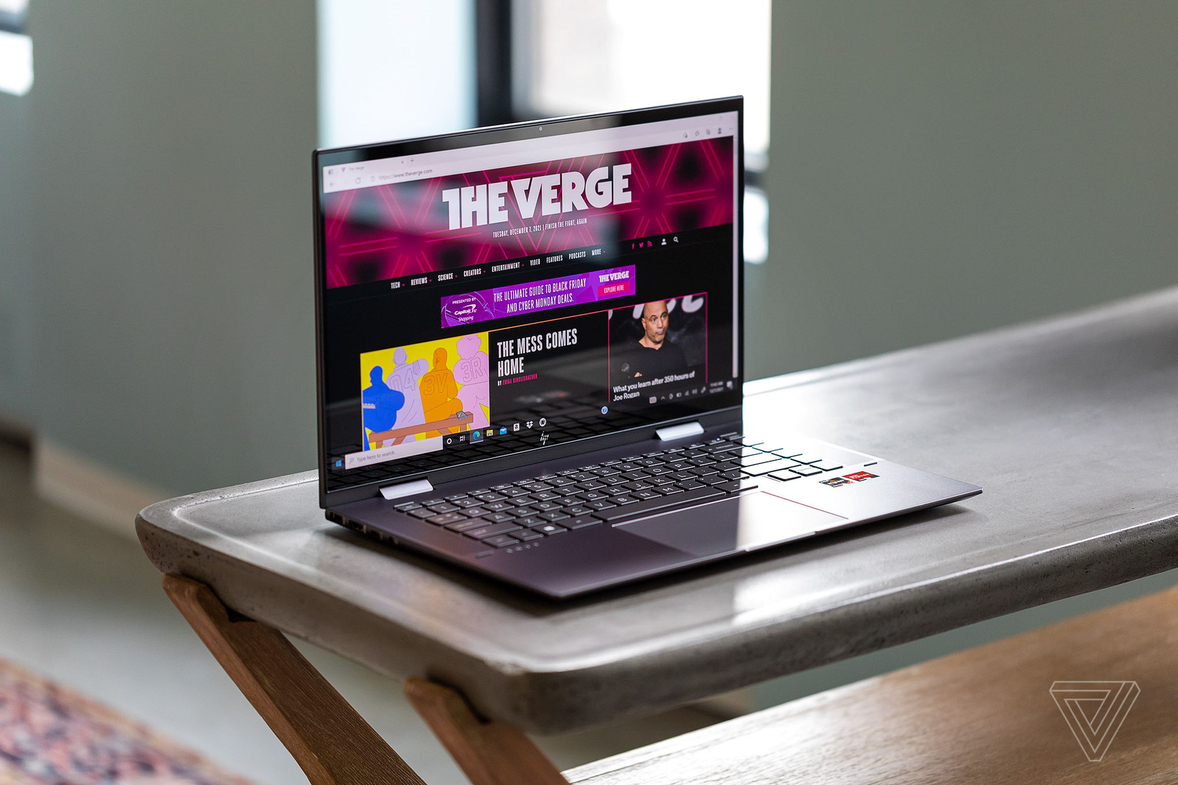 The HP Envy x360 15 on a table seen from above and to the left. The screen displays The Verge homepage.