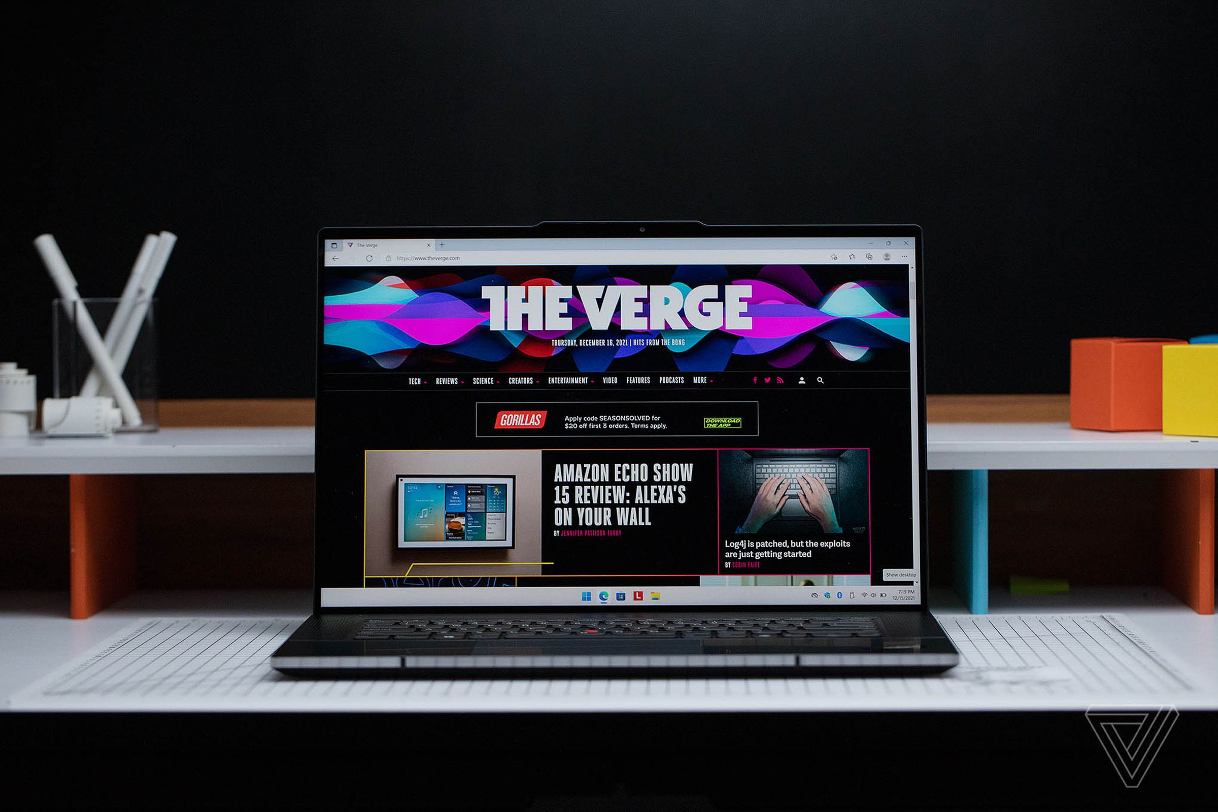 The ThinkPad Z16 open on a gridded table with a black background. The screen displays The Verge homepage.