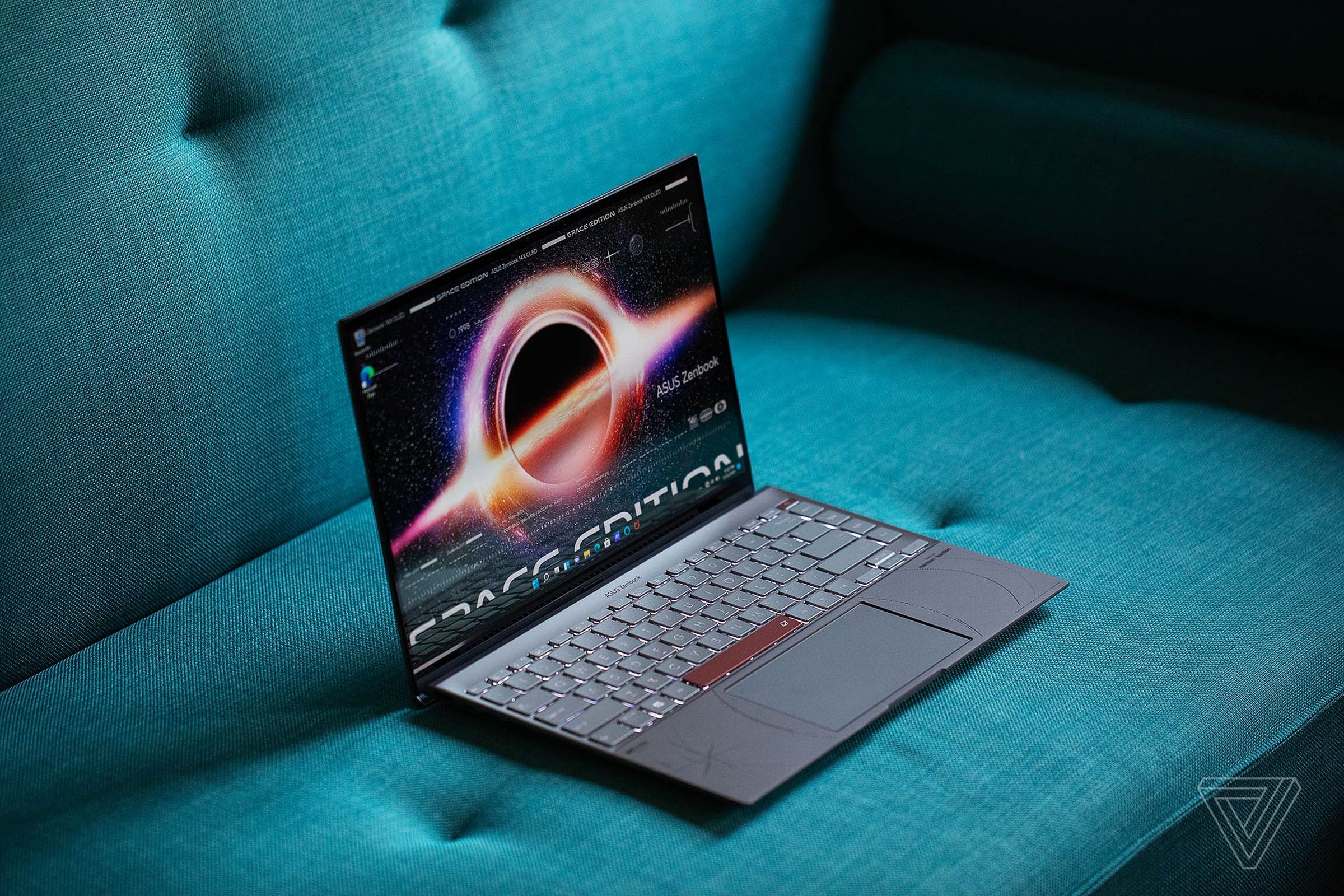 The Asus Zenbook 14 OLED Space Edition on a green couch angled to the right, open, from above. The screen displays a supernova with the words Space Edition across the bottom.