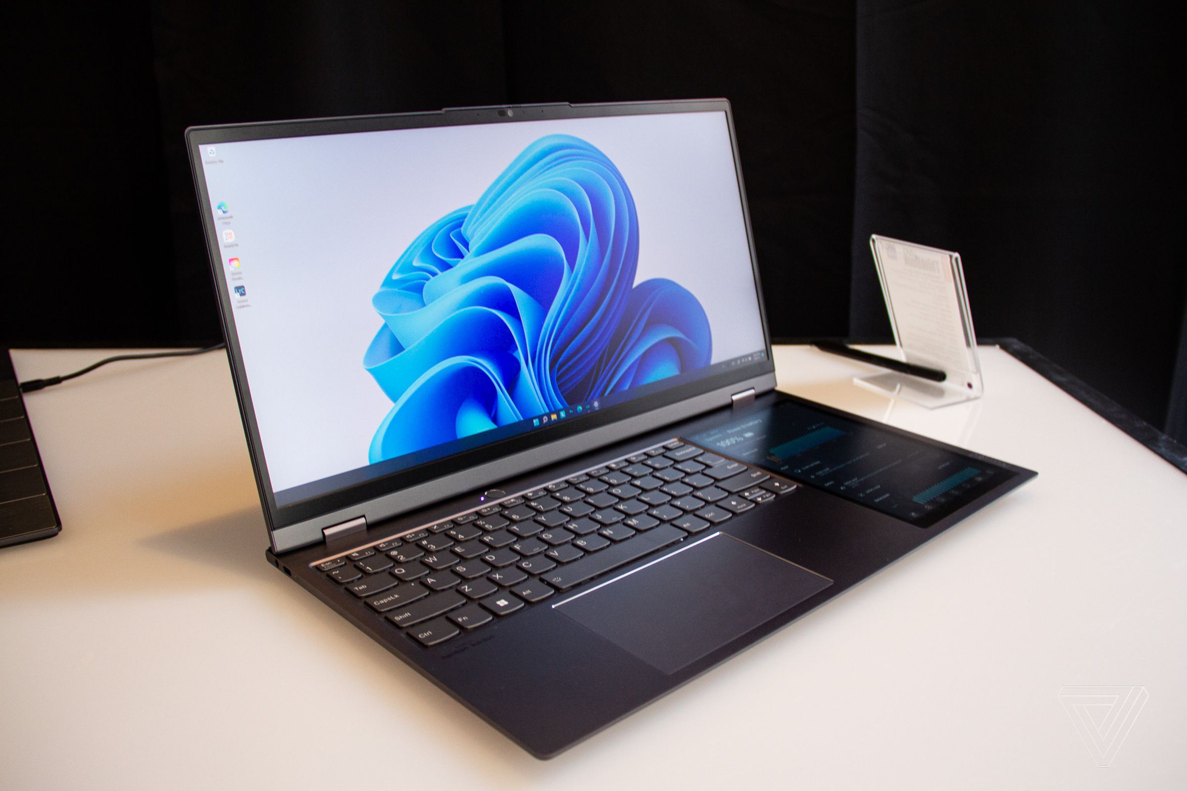 The ThinkBook Plus Gen 3 open on a table angled to the right. The primary screen displays a blue swirl on a white background.