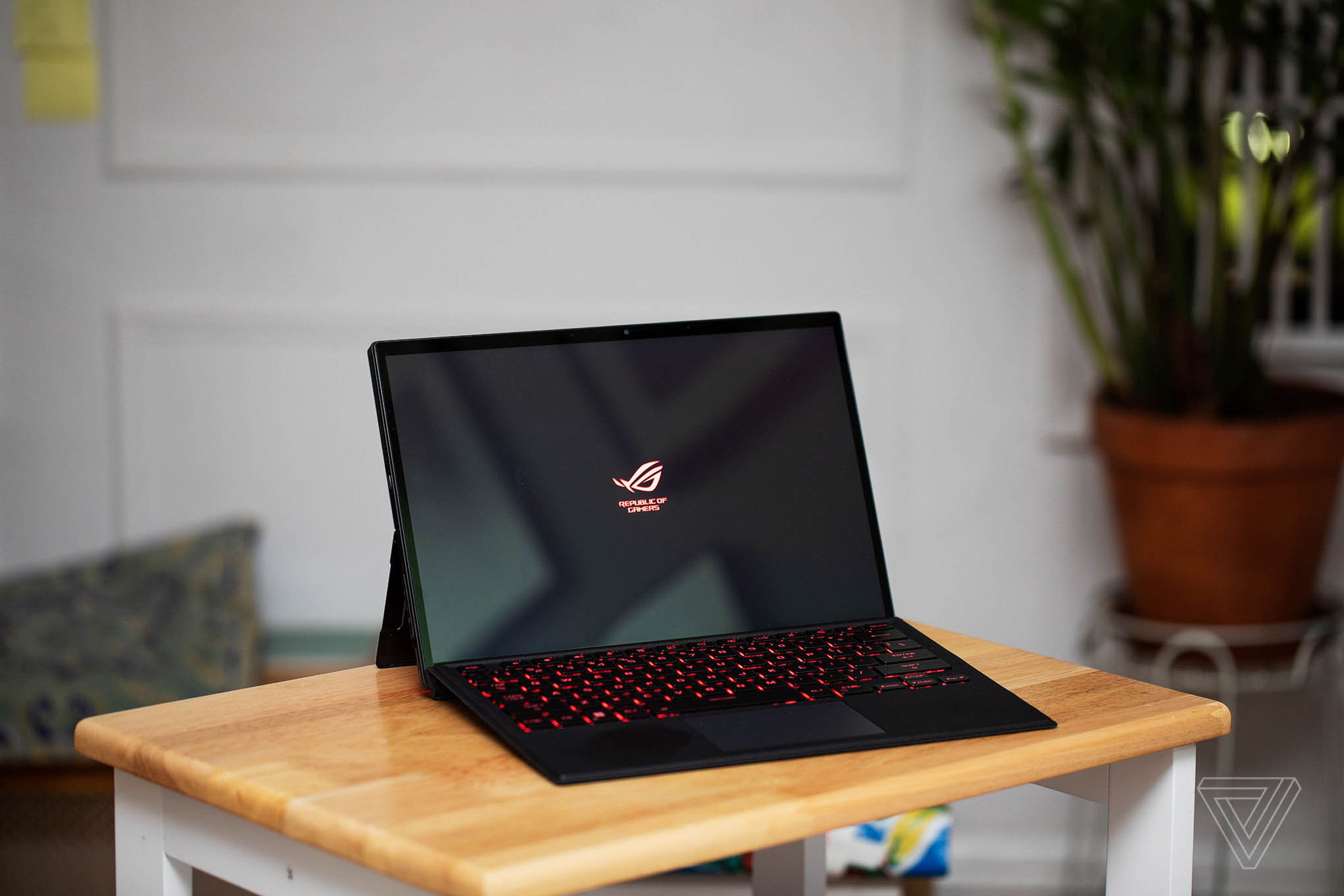 The Asus ROG Flow Z13 in laptop mode on a small table. The screen displays the ROG logo.