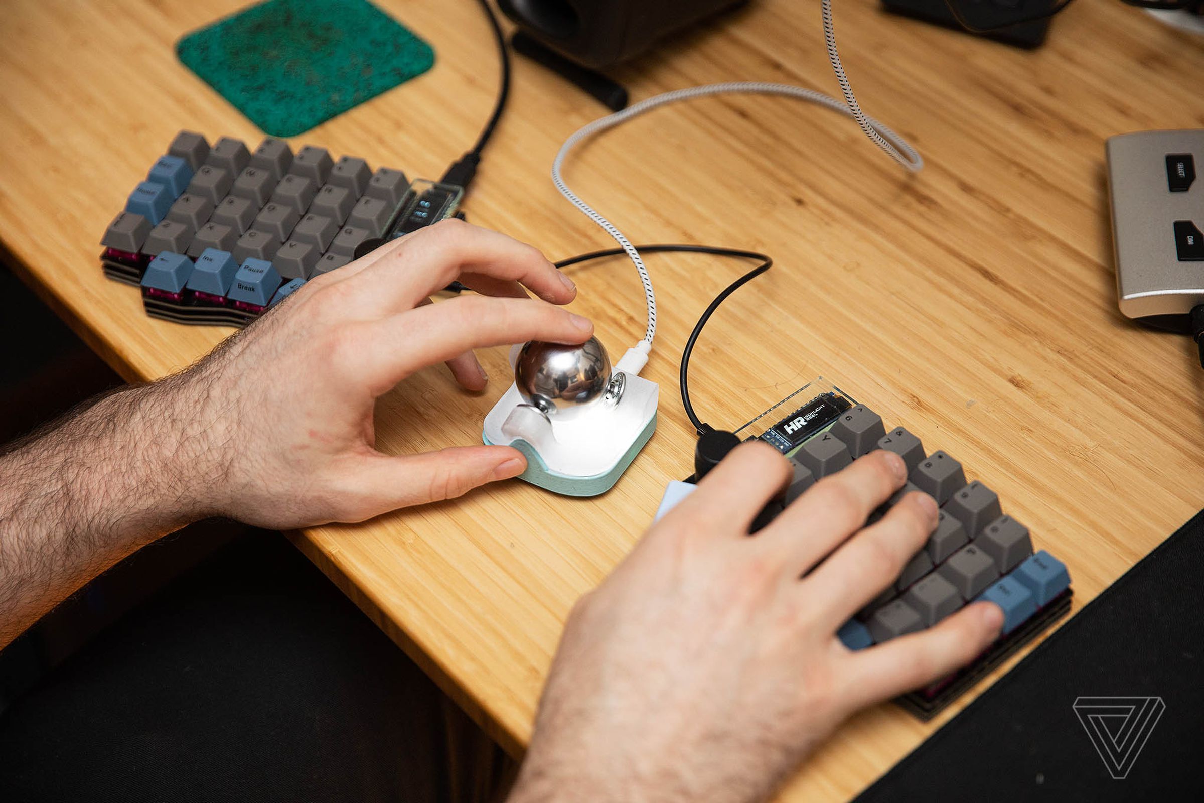 A man using a split keyboard with a trackball between the two halves. It features a large, shiny metal ball bearing.
