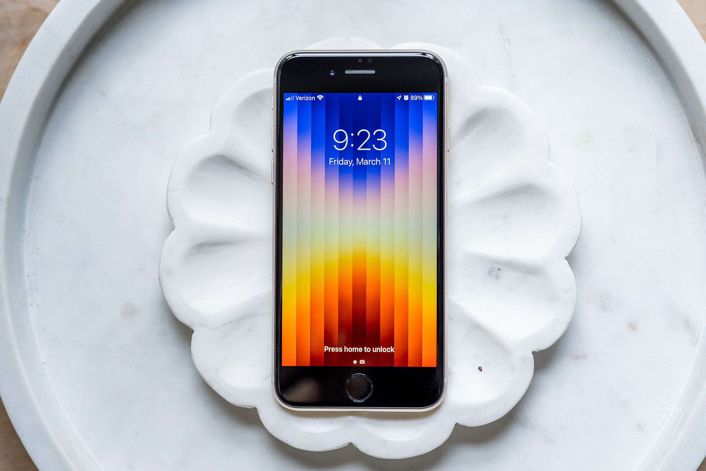 iPhone SE with screen side up showing colorful lock screen wallpaper.