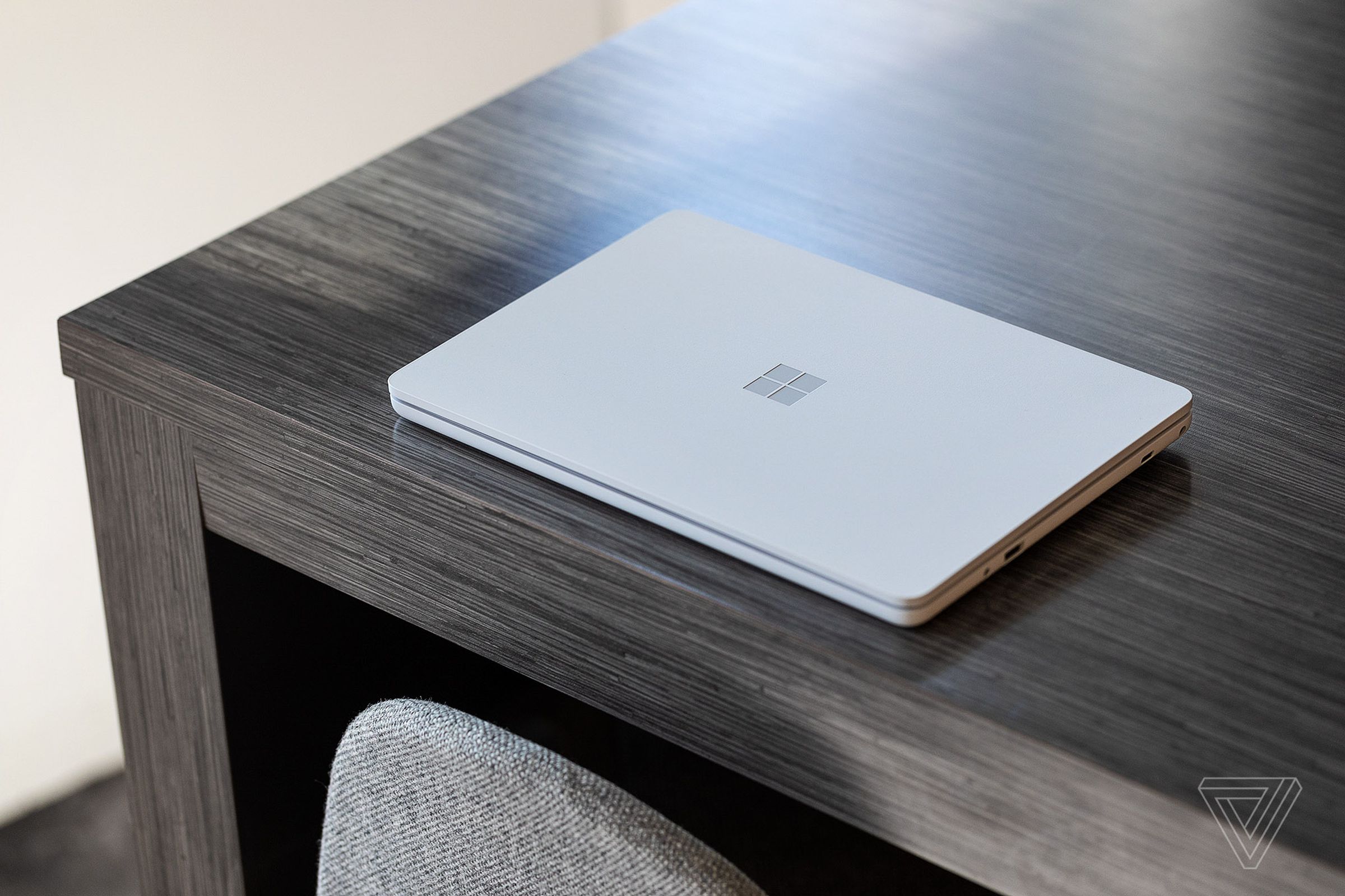 The Surface Laptop SE closed, seen from above, on the edge of a wooden table.