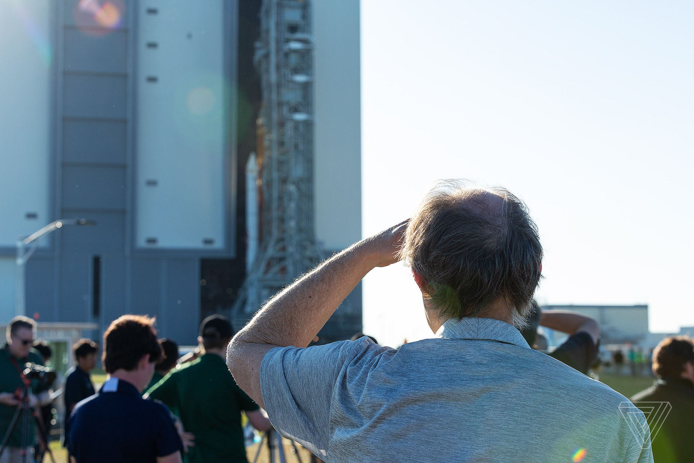 An onlooker shields his eyes while looking at the SLS emerging form the VAB.