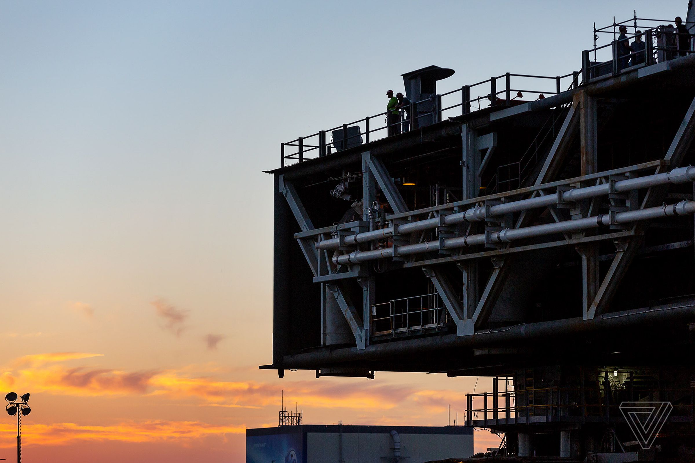 The Sun sets behind the mobile launch platform, as workers look over the edge.