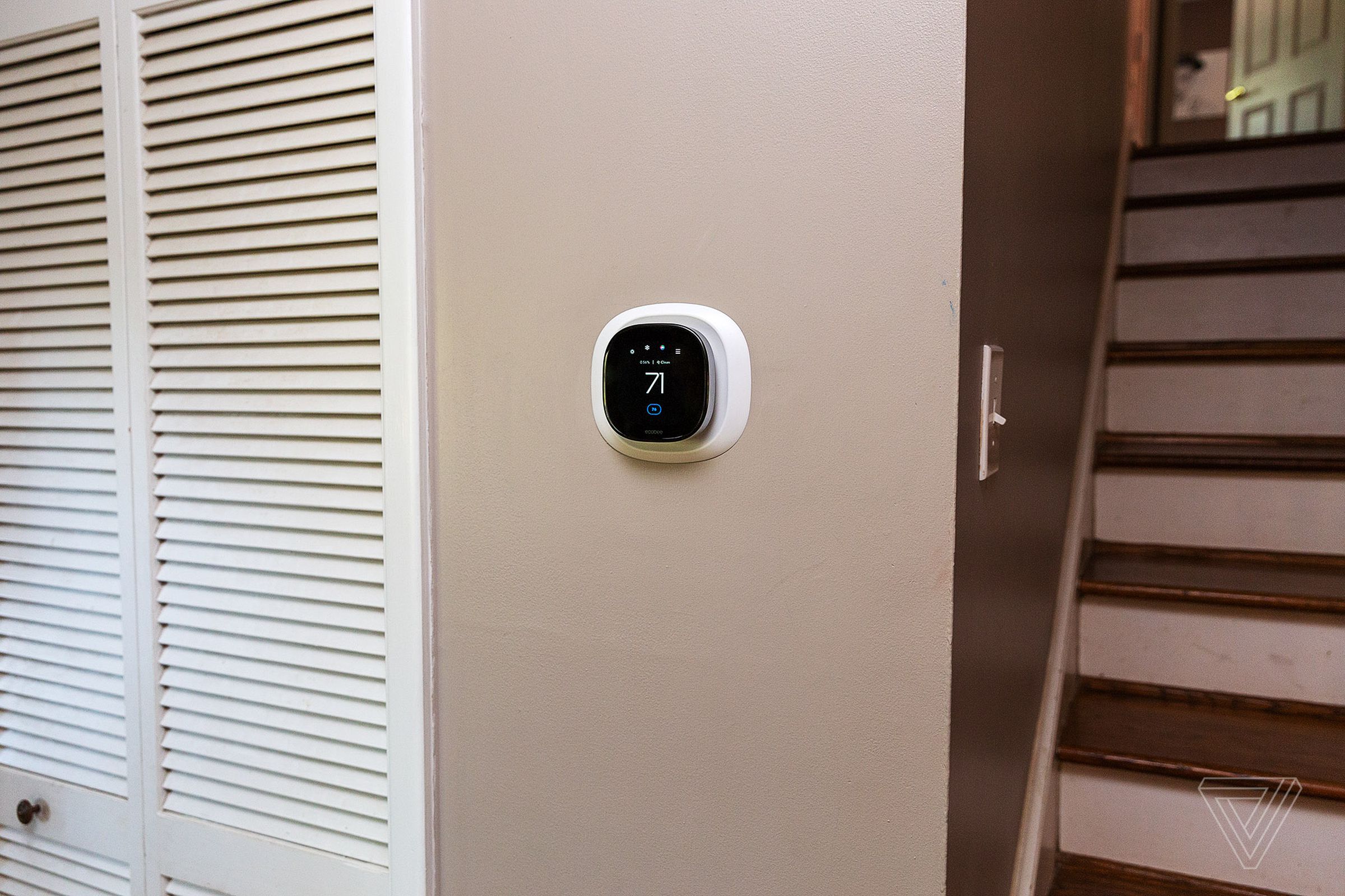 Small Ecobee thermostat on a tan wall in between closet and staircase.
