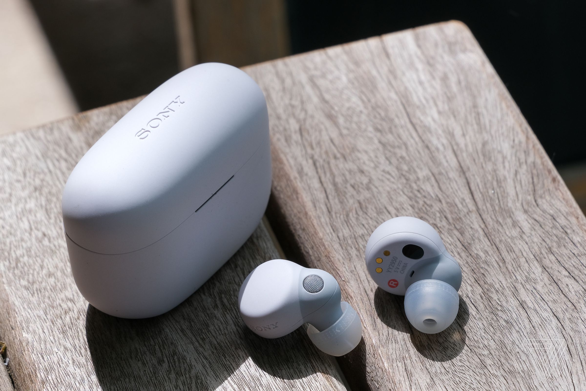 The white Sony LinkBuds S wireless earbuds and their charging case sitting on the edge of a wood table.