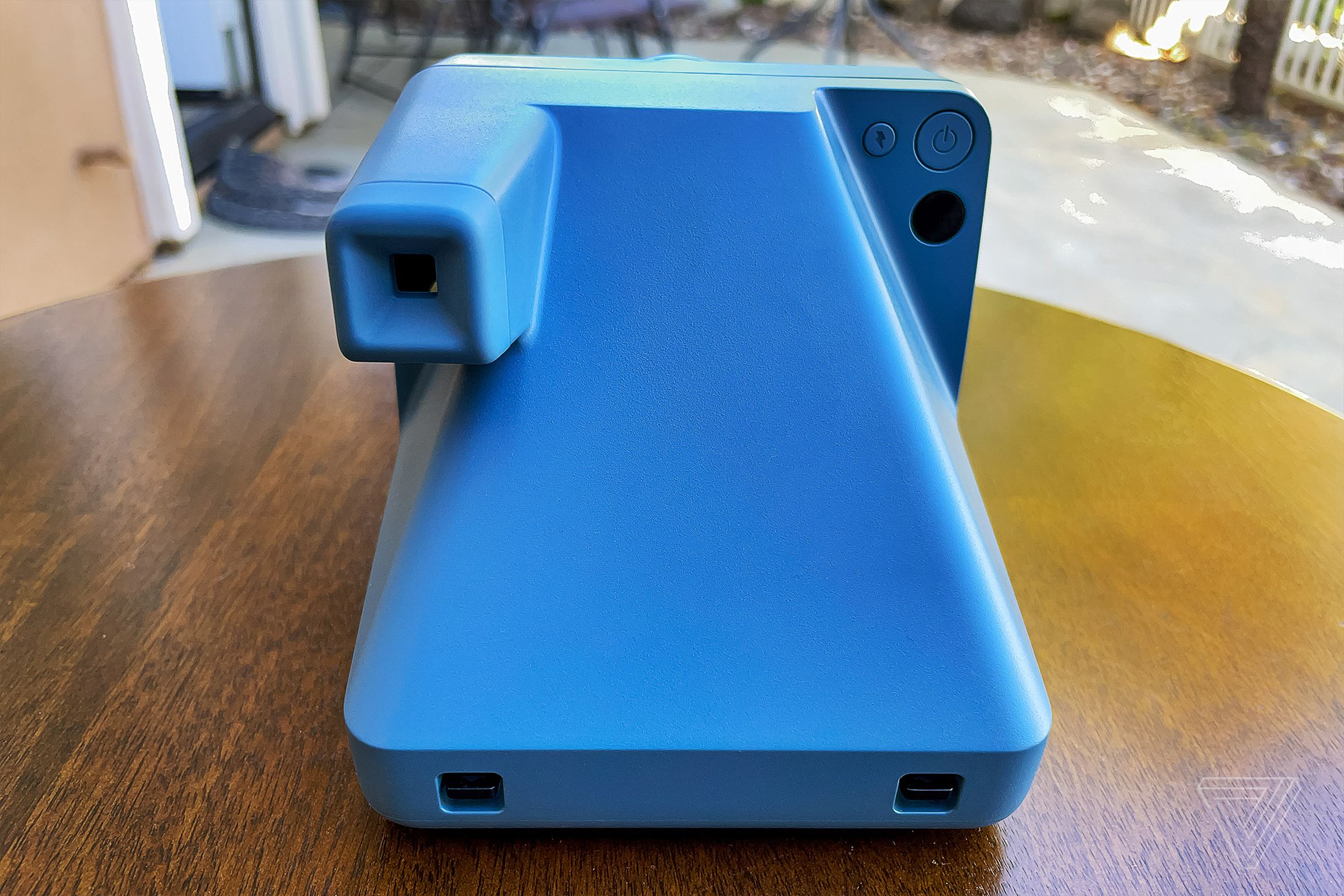 The back of the blue Polaroid Now Plus resting on a table with its viewfinder.