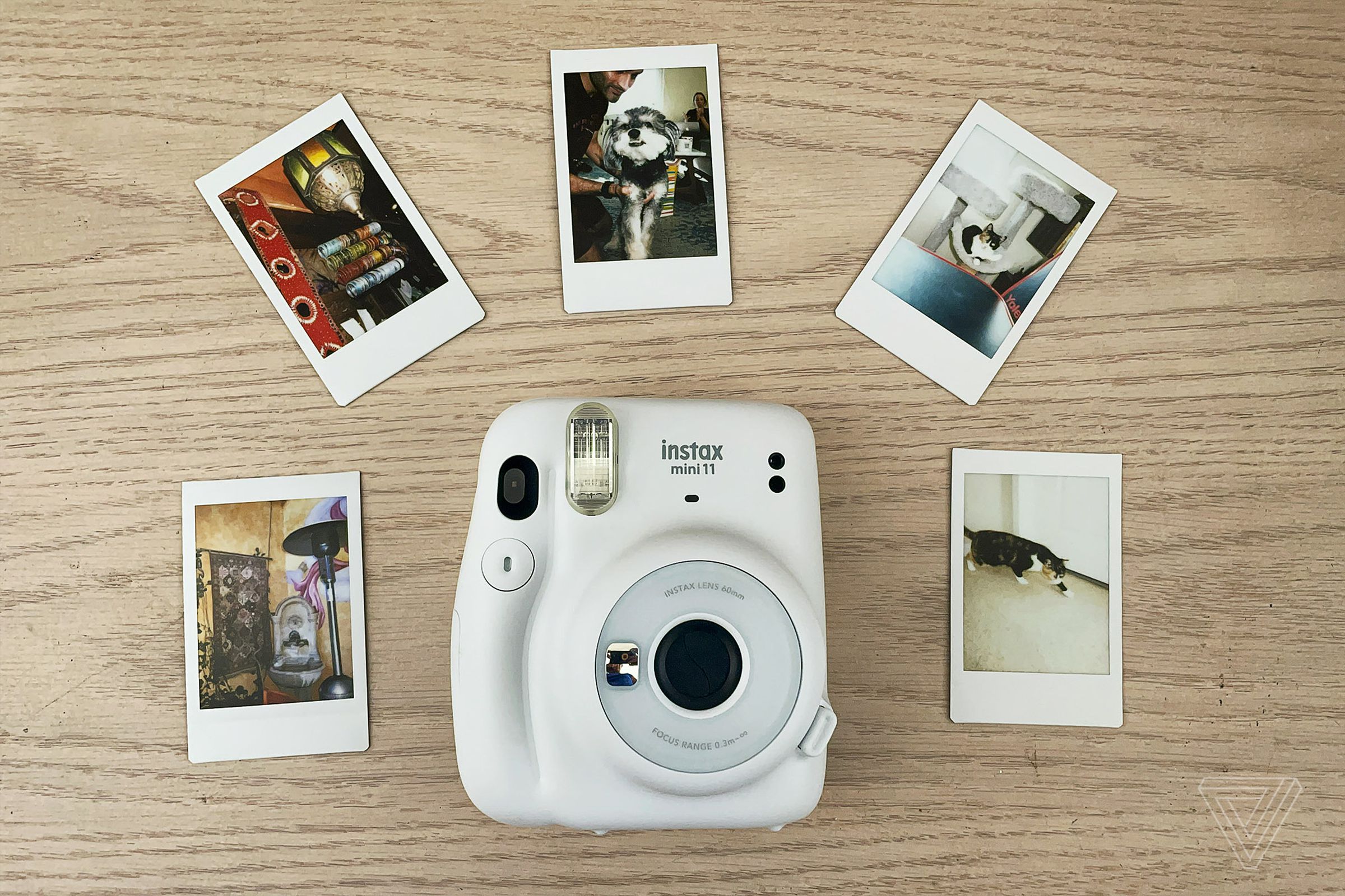 The Instax Mini 11 in the middle rest on a table surrounded by five photos it’s produced.