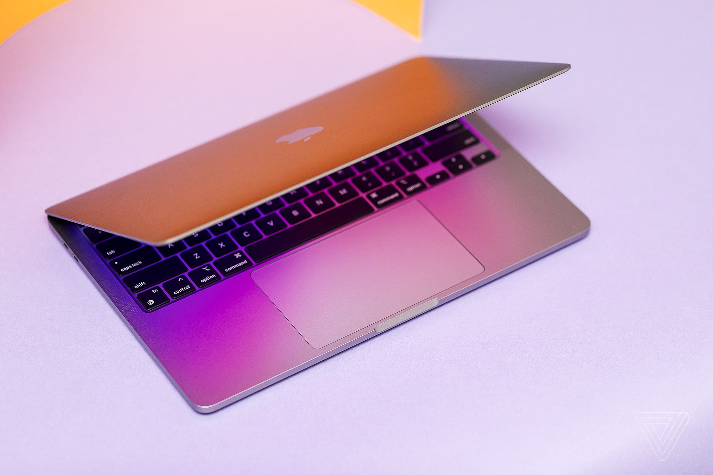 The MacBook Pro 13 2022 half open seen from above on a lavender background.