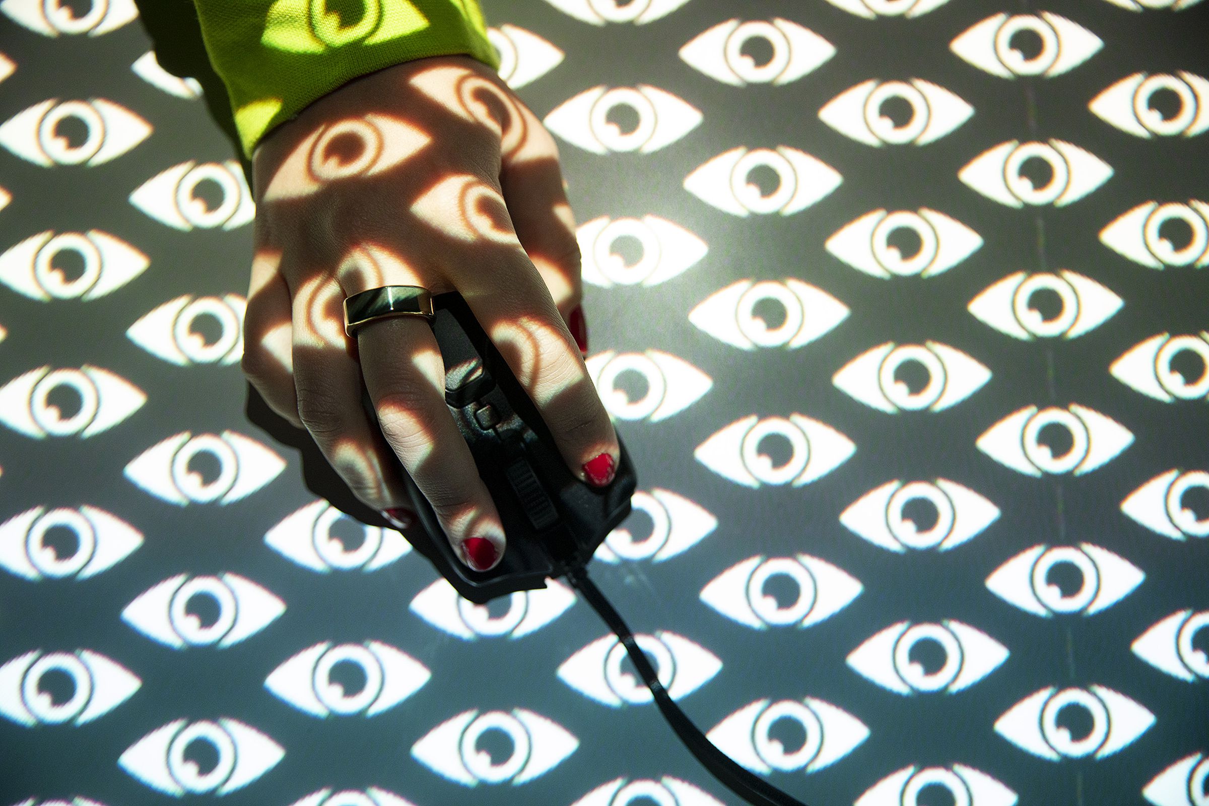The image shows a hand operating a computer mouse behind an illustrated pattern of eyes.