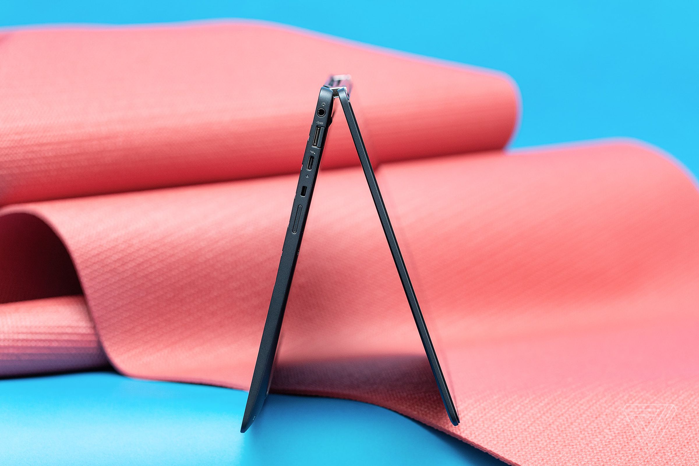 The HP Elite Dragonfly Chromebook folded backwards in tent mode, seen from the side on a blue and pink background.