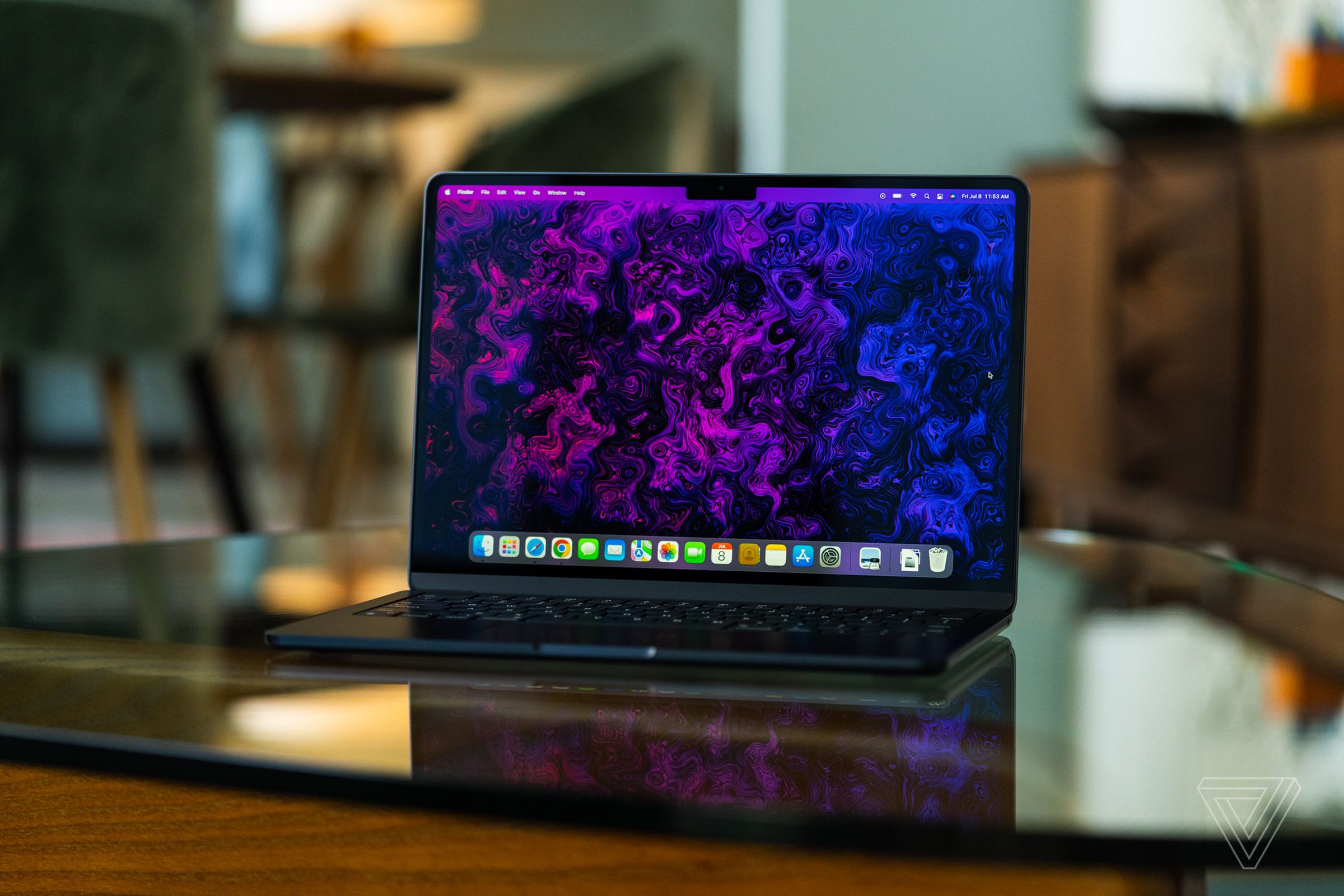 MacBook Air M2 открыт, лицом к камере.  Его дисплей включен, демонстрируя психоделические пурпурно-черные обои, созданные командой художников и иллюстраторов The Verge.
