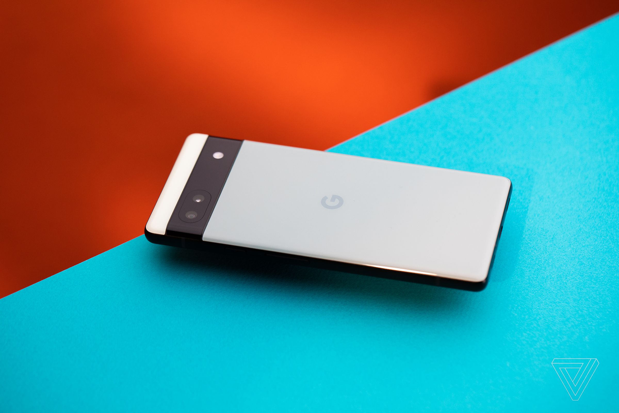 Google’s Pixel 6A sits face down on a blue and red backdrop. This shot reveals the phone’s backside, including its cameras, and Google’s G logo.