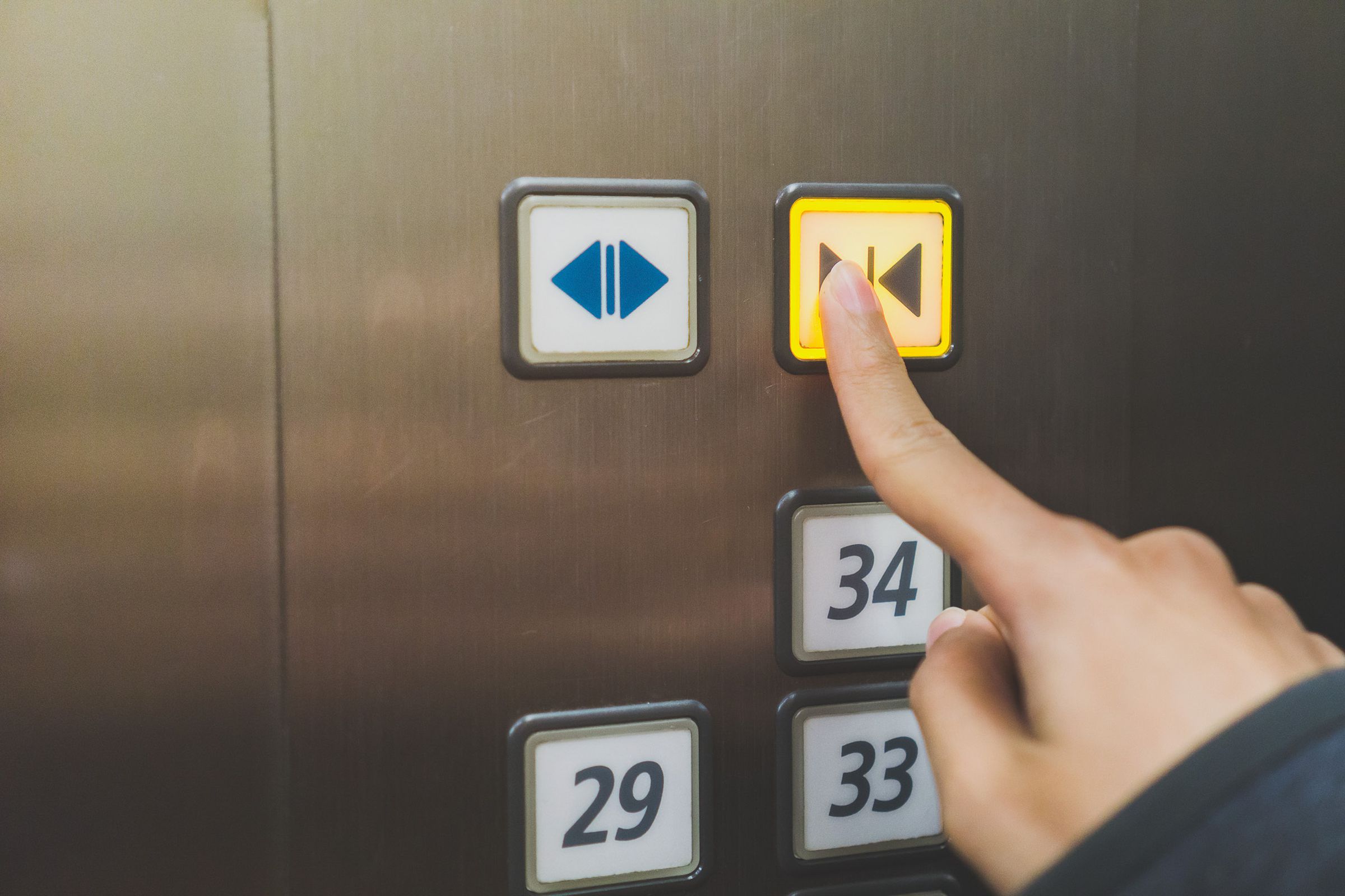 Image of someone pressing the close door button in an elevator.