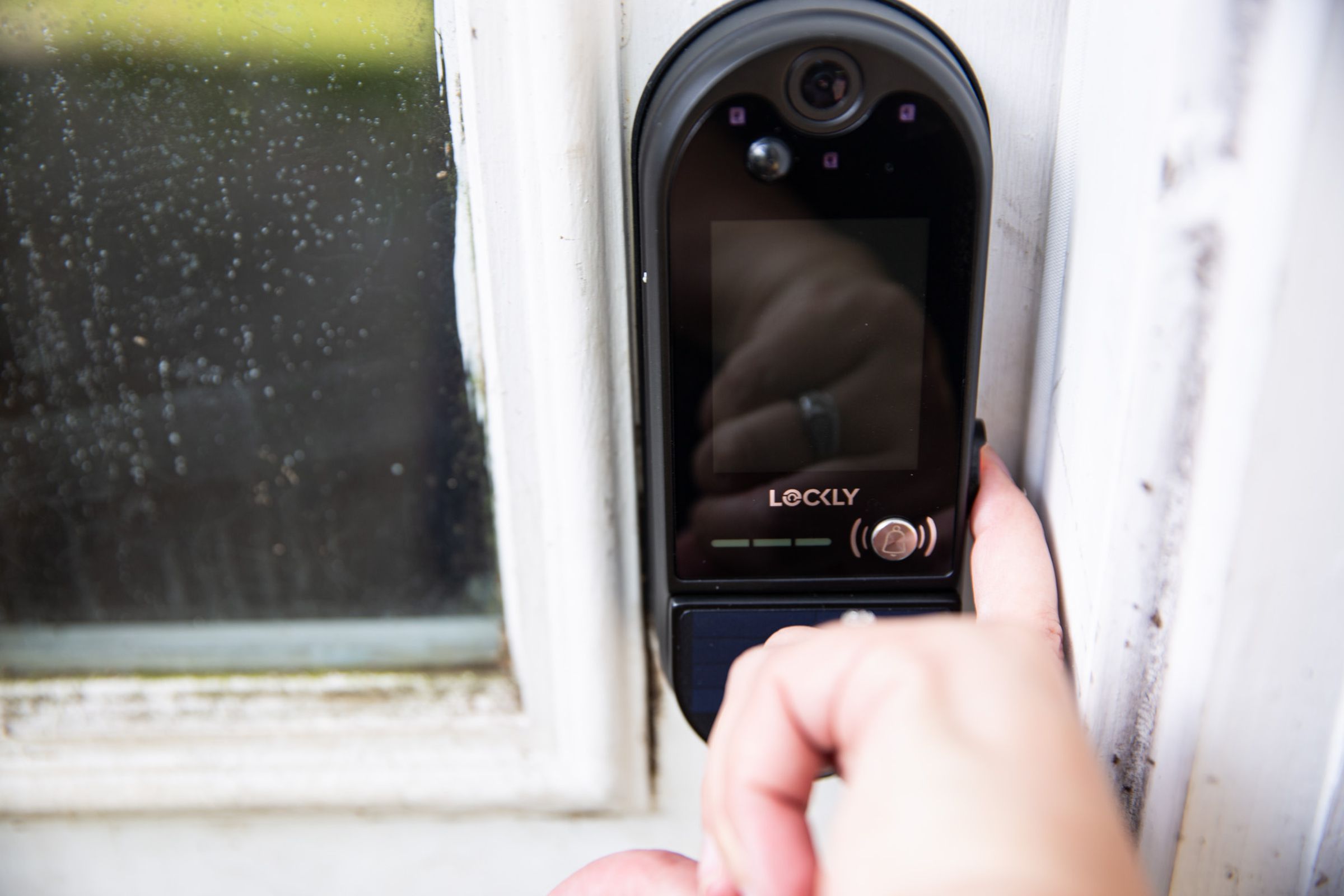 Photo of the Lockly Vision Elite installed on the right-hand side of a door. A person is trying to use the fingerprint reader and has wedged their finger between the lock and the jamb in trying to do so.