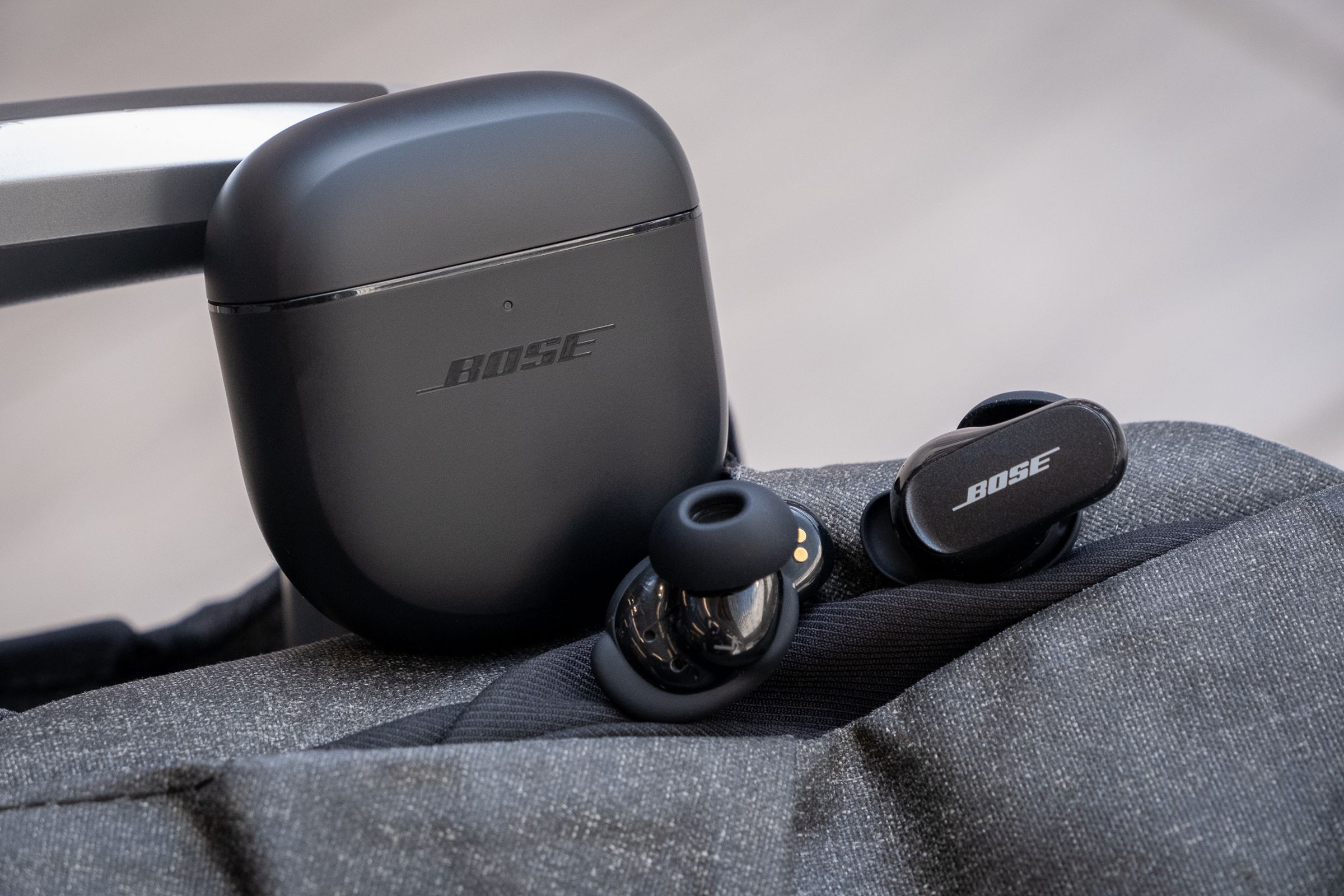 The Bose QuietComfort Earbuds II sitting beside their case on top of a travel bag.