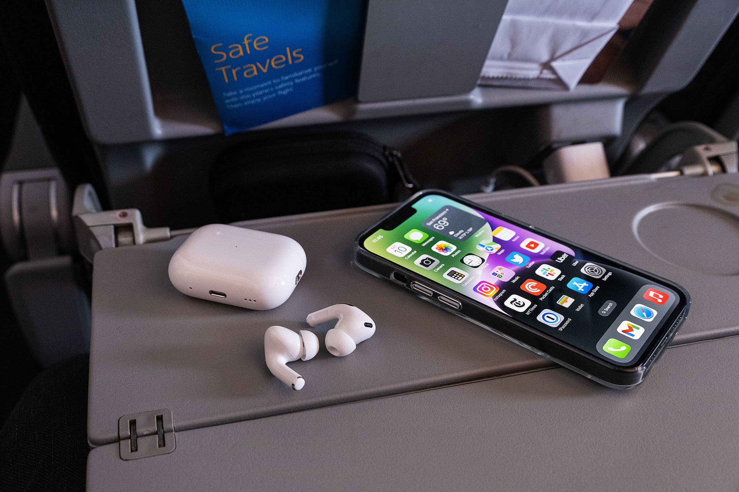 Le AirPods Pro di seconda generazione di Apple raffigurate sul tavolino di un aereo accanto a un iPhone 14.