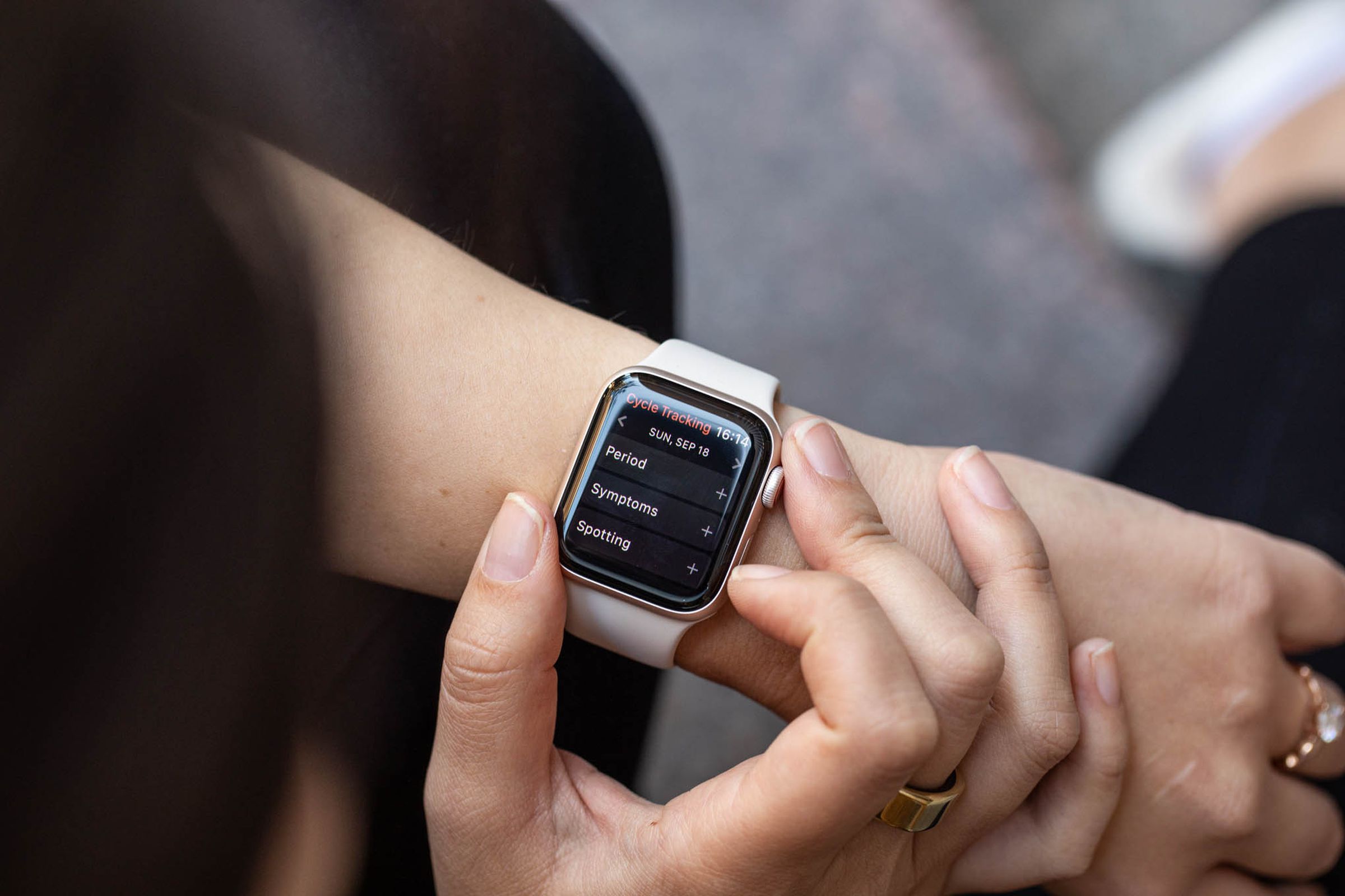 An Apple watch on a wrist showing a screen with cycle tracking options like “period” and “symptoms”