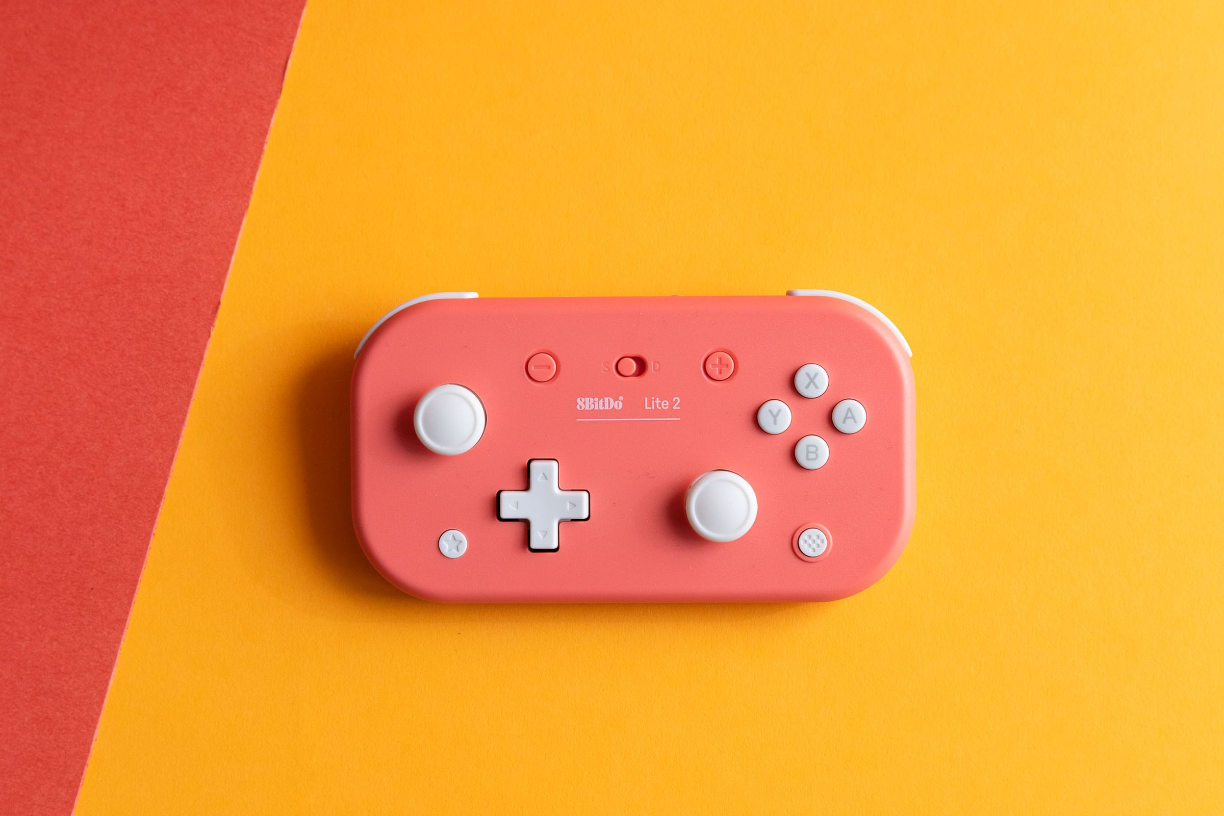 The pink 8BitDo Lite 2 wireless controller for the Nintendo Switch and other platforms sitting on a yellow and red back drop.
